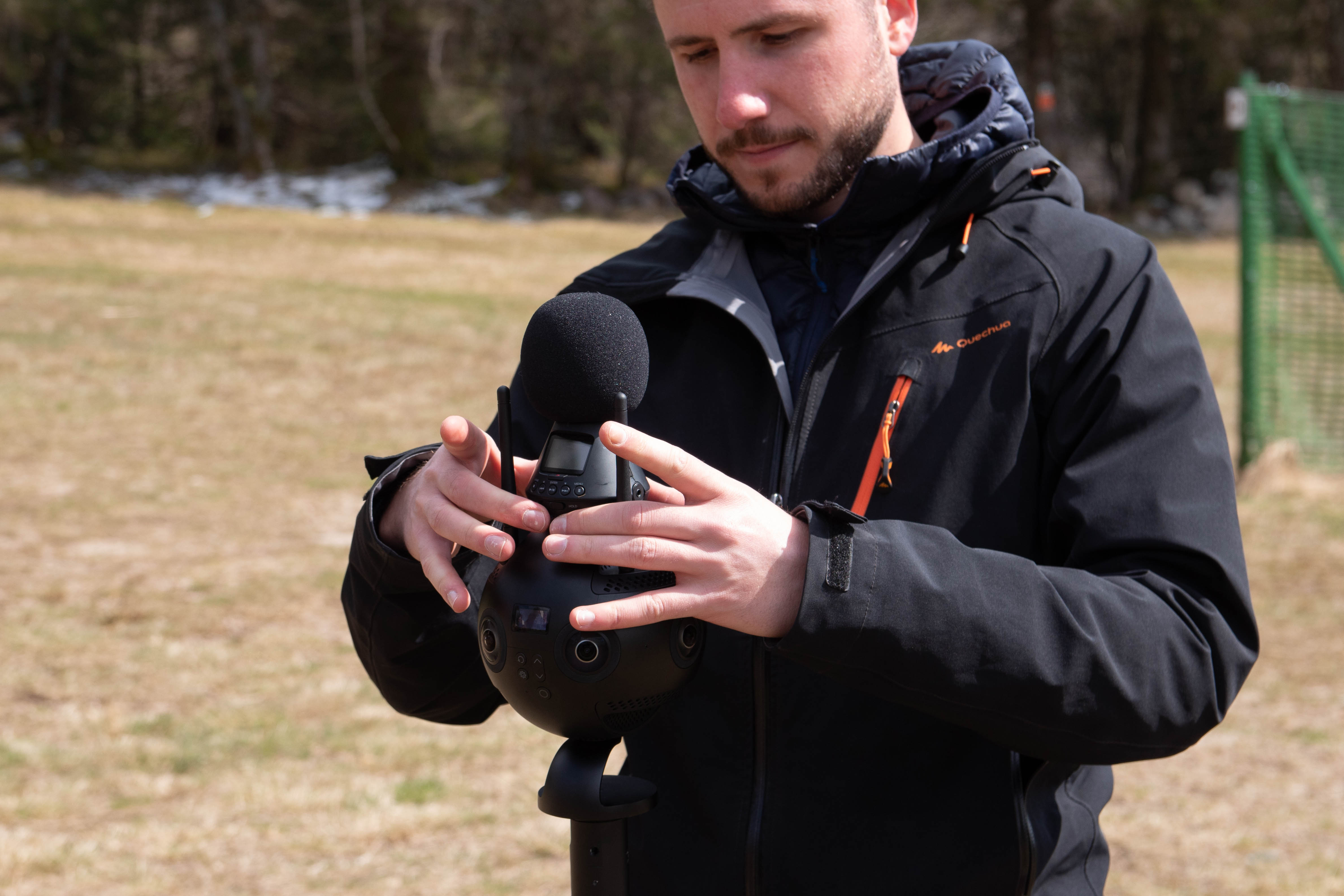 A person stands against a vibrant background of orange and yellow wavy patterns. They are wearing a dark coat, looking contemplative and thoughtful.