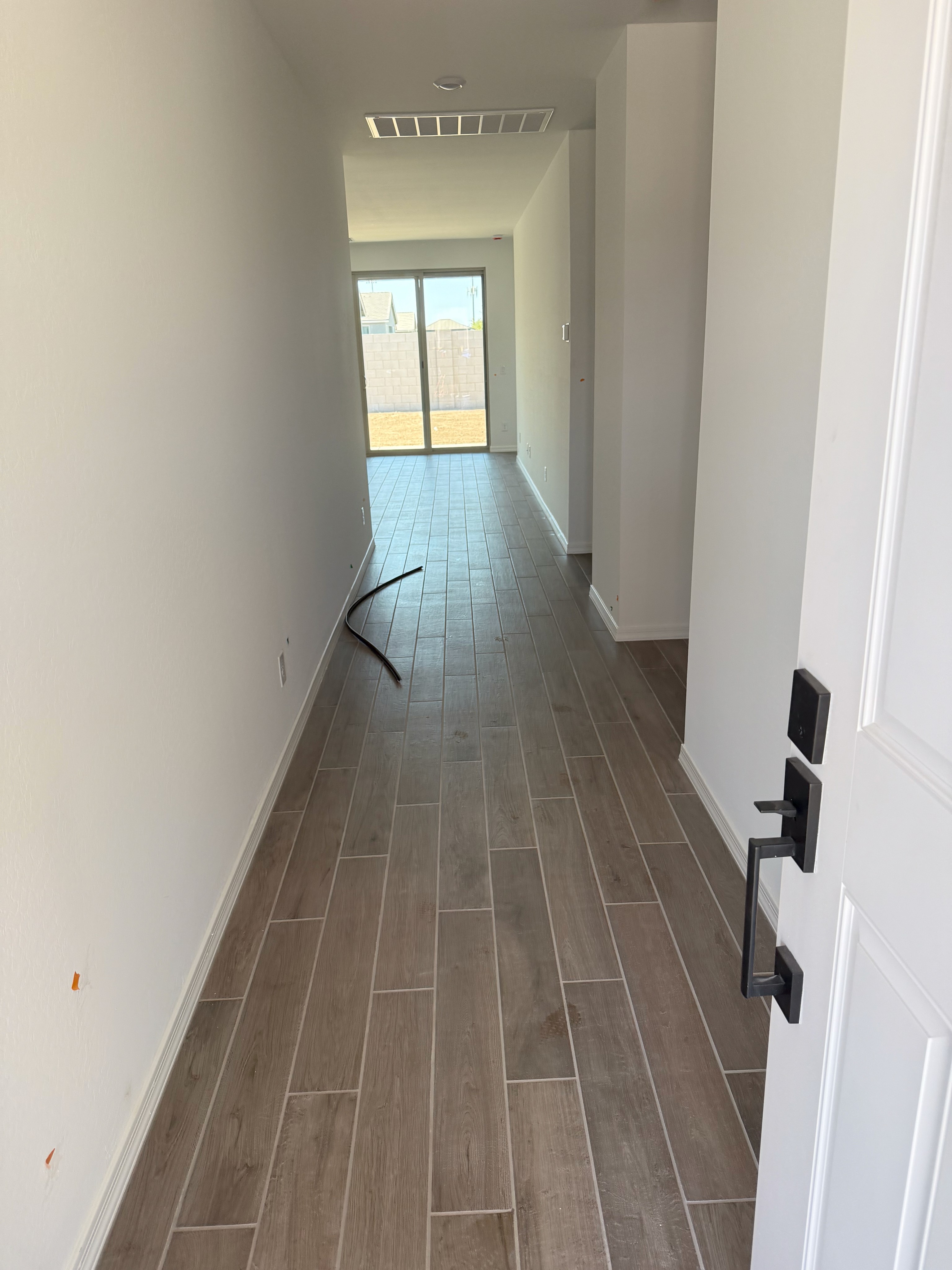 Modern hallway with wood-look tile flooring, large sliding glass doors, and white walls in a new home under construction.