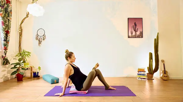 Pregnant woman in a prop-supported hip-opening yoga pose – prenatal yoga class to create lower body space and improve hip mobility for birth preparation