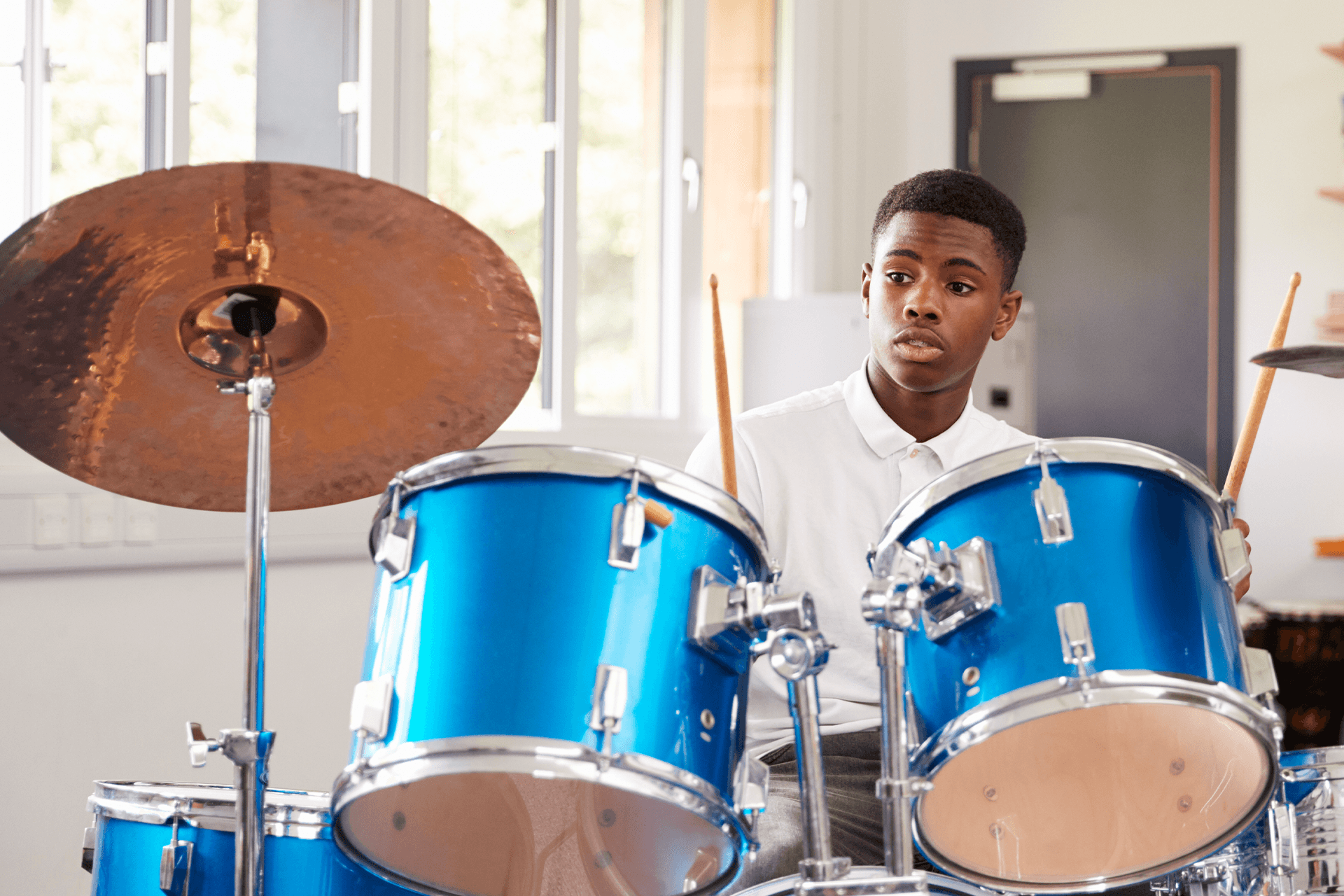 Teenager learning to play the drums, focused on practicing the mentor's instructions in a music classroom