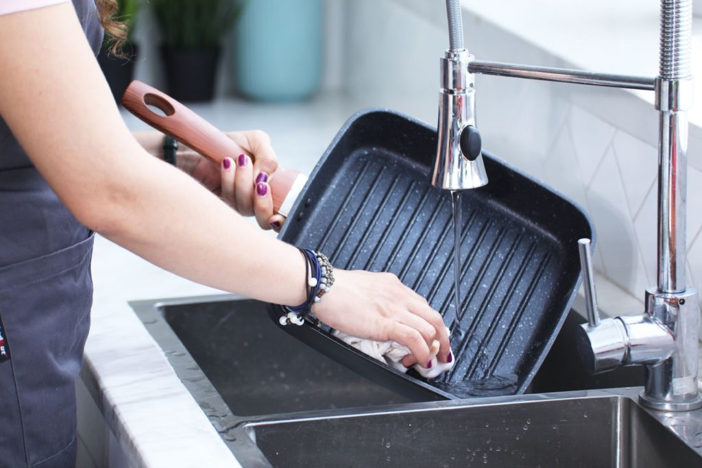 A person washing a pan in the kitchen sink. Photo by Cooker King on Unsplash.