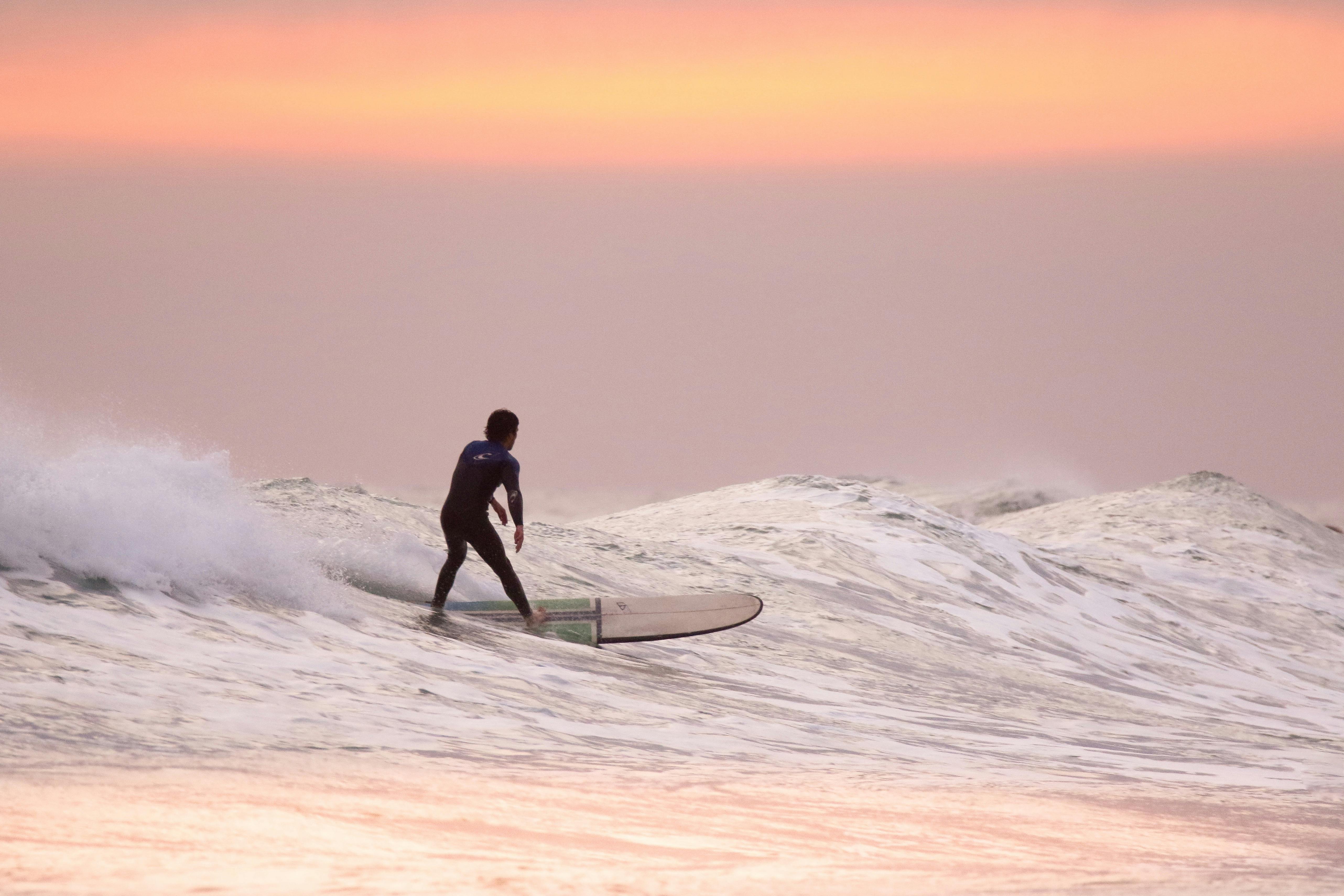 Surfer on a wave with a pink and orange sky.