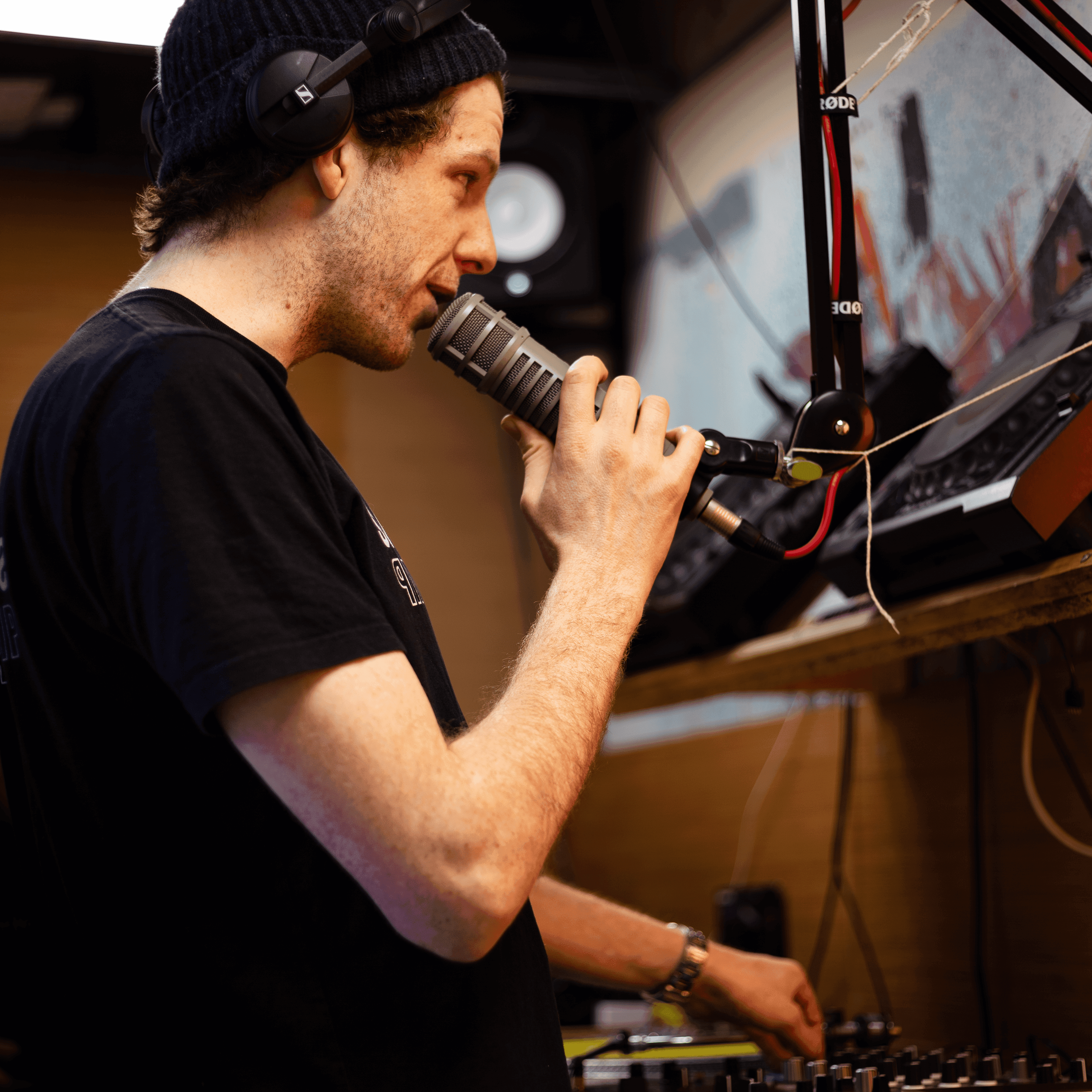 Man holding a microphone while stood in front of dj equipment at Noods radio station