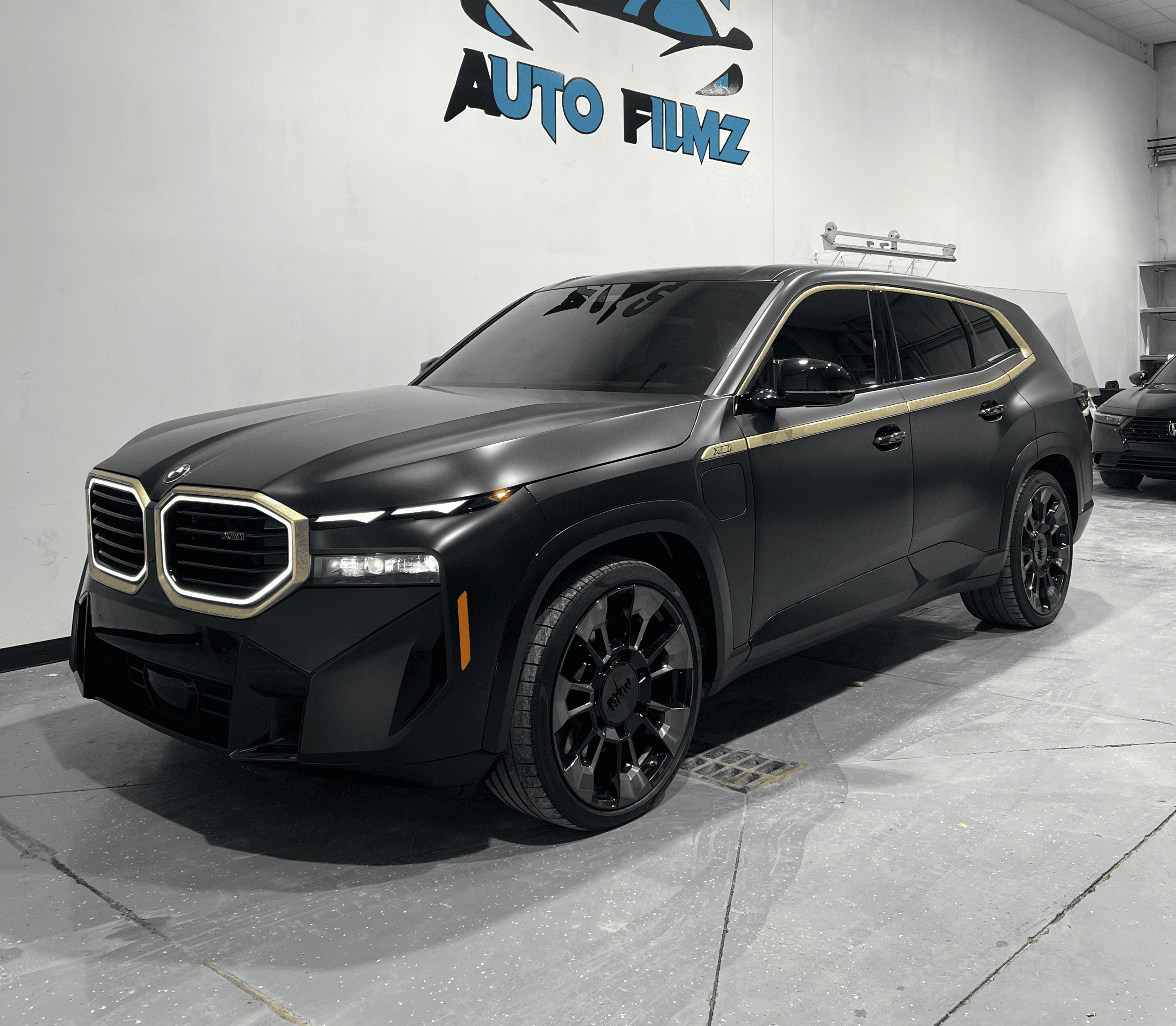 A matte black BMW XM luxury SUV is parked indoors on a polished concrete floor.