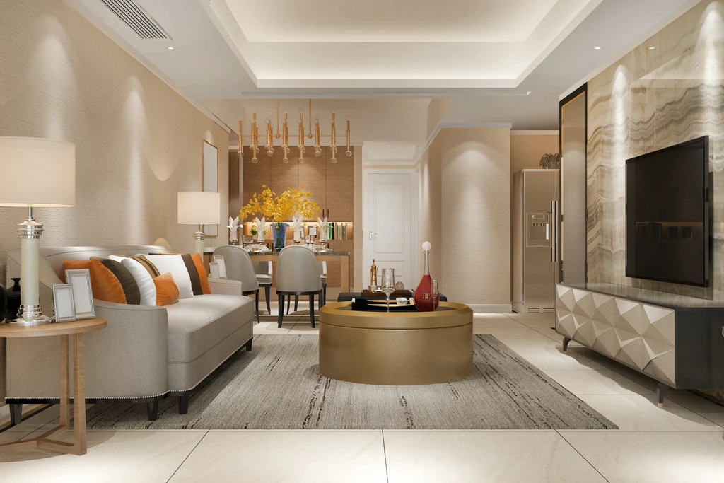 Modern living room with beige walls and sleek furniture. Features a gray sofa with colorful pillows, oval coffee table, TV, and dining area with flowers. Elegant and cozy ambiance.