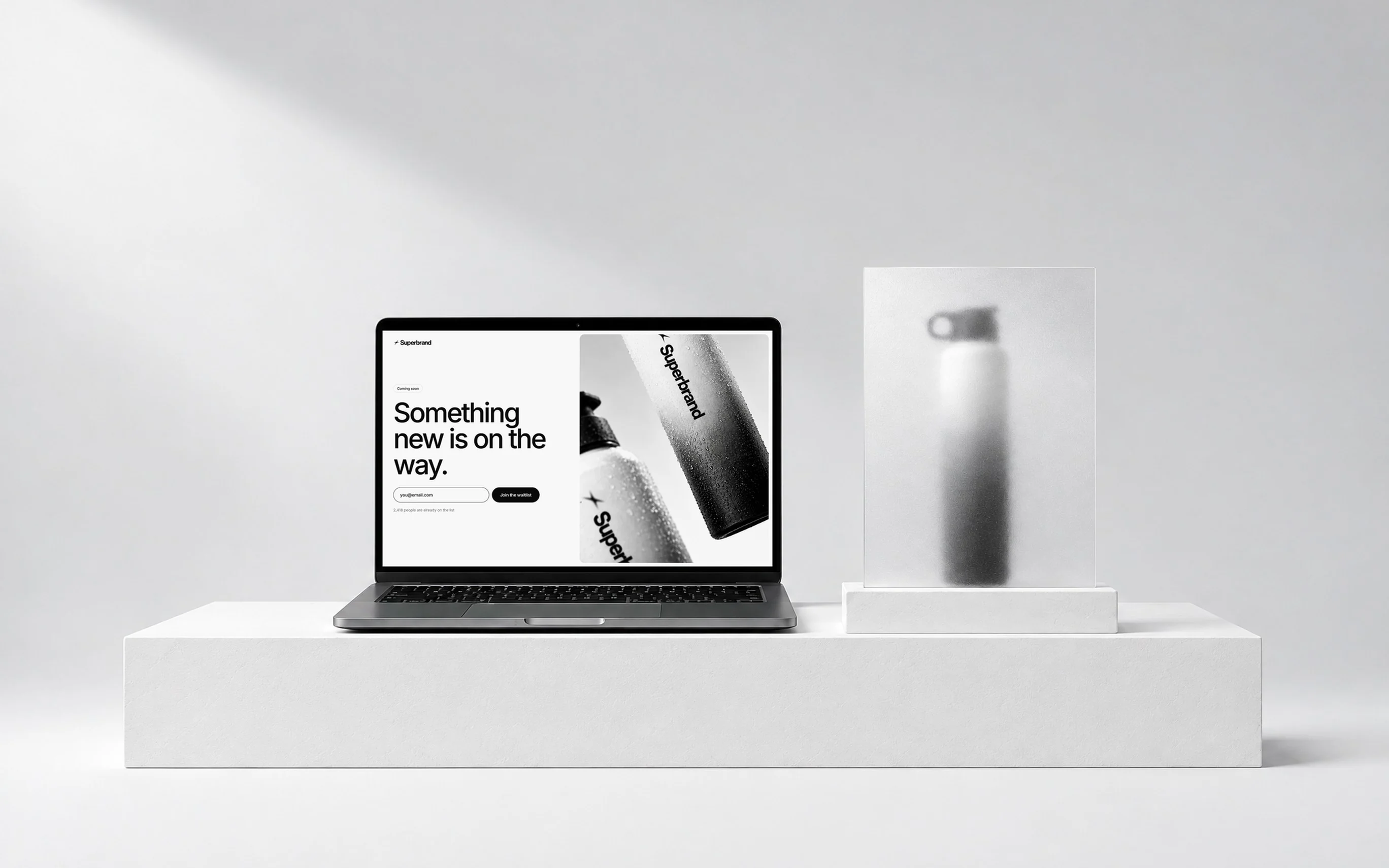 A laptop showing a Superbrand prelaunch page, “Something new is on the way.”, beside a bottle behind frosted glass.