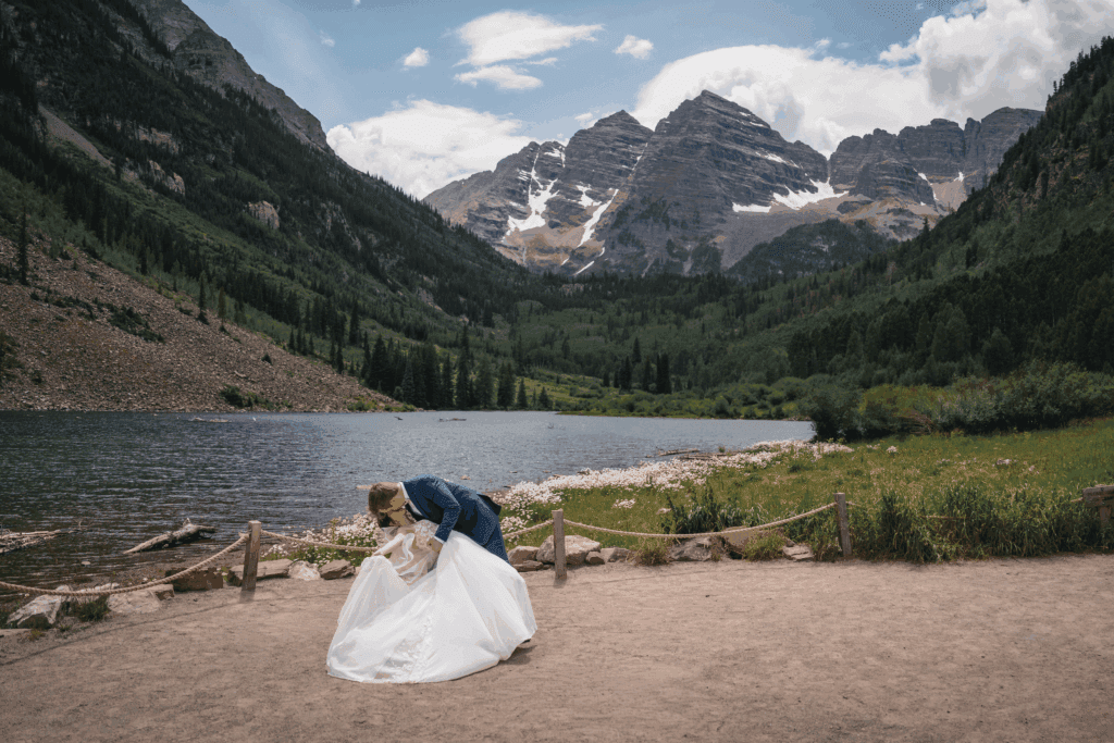 Groom dipping his bride in front of the Maroon Bells with alpine peaks in the background.