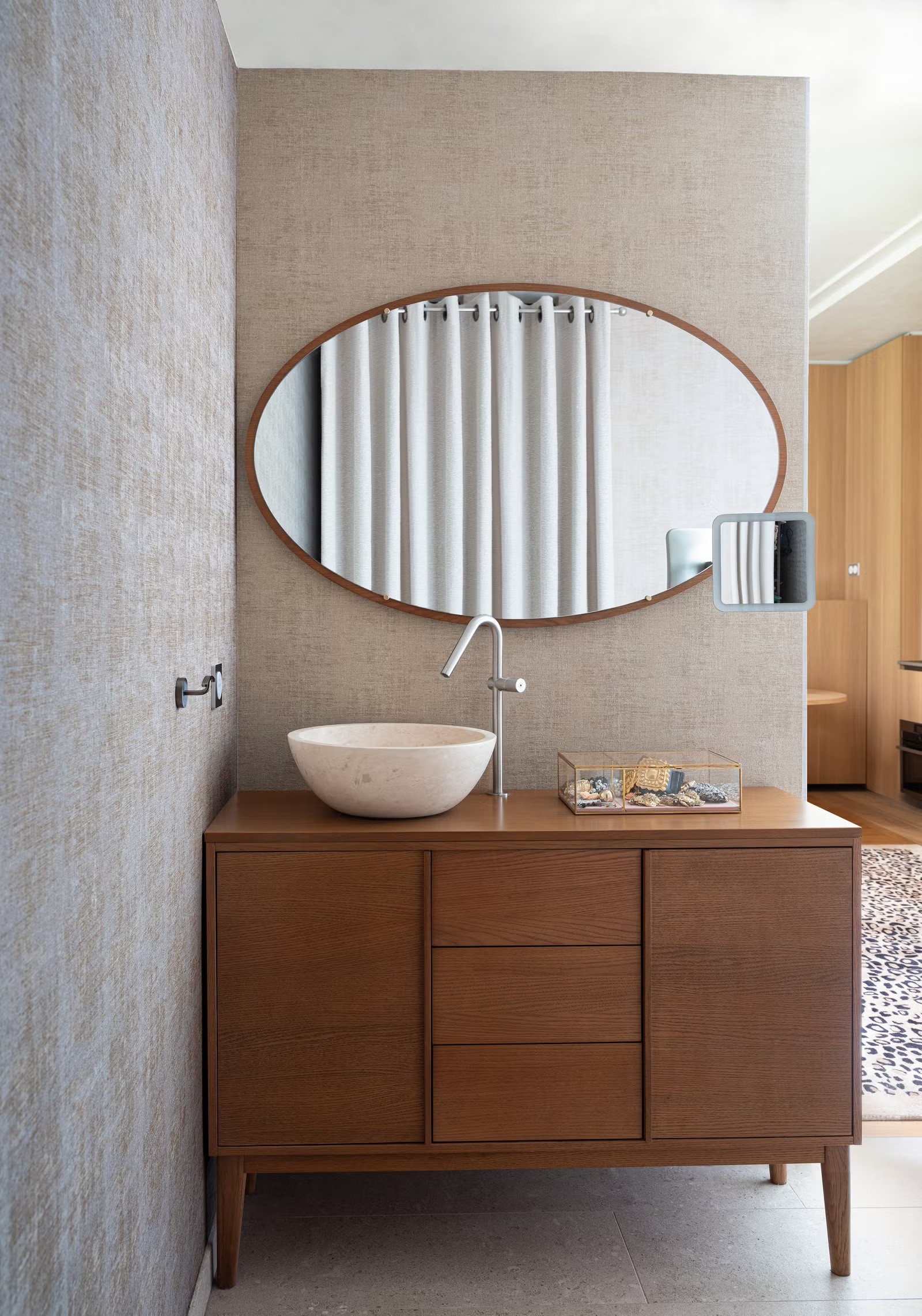 Salle de bain de luxe avec vasque à poser blanche sur meuble en bois noble et grand miroir ovale rétro-éclairé.