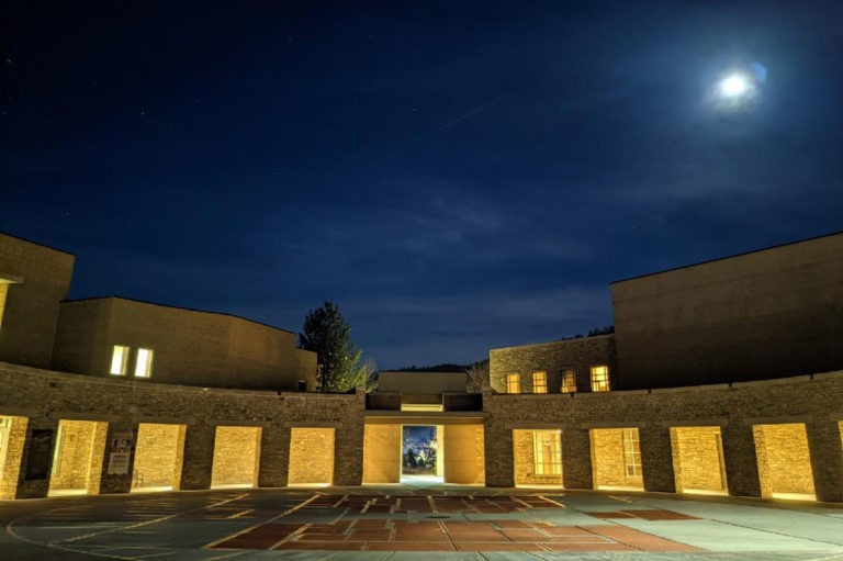 Exterior courtyard at night with moon visible above building, emphasizing relationship between architecture, sky, and celestial cycles