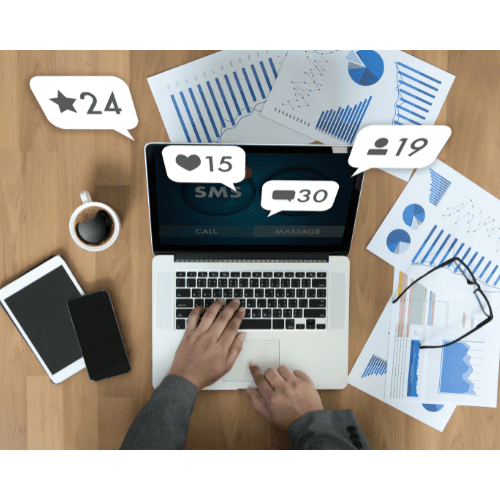Laptop with SMS marketing screen, analytics papers, and engagement counters.