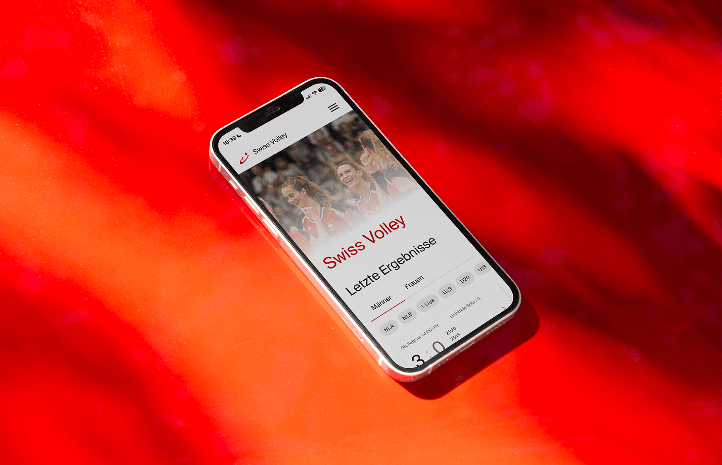 iPhone 13 laying on a red background showing the website "Swiss Volley". On the Website there's a header showing volleyball players celebrating.