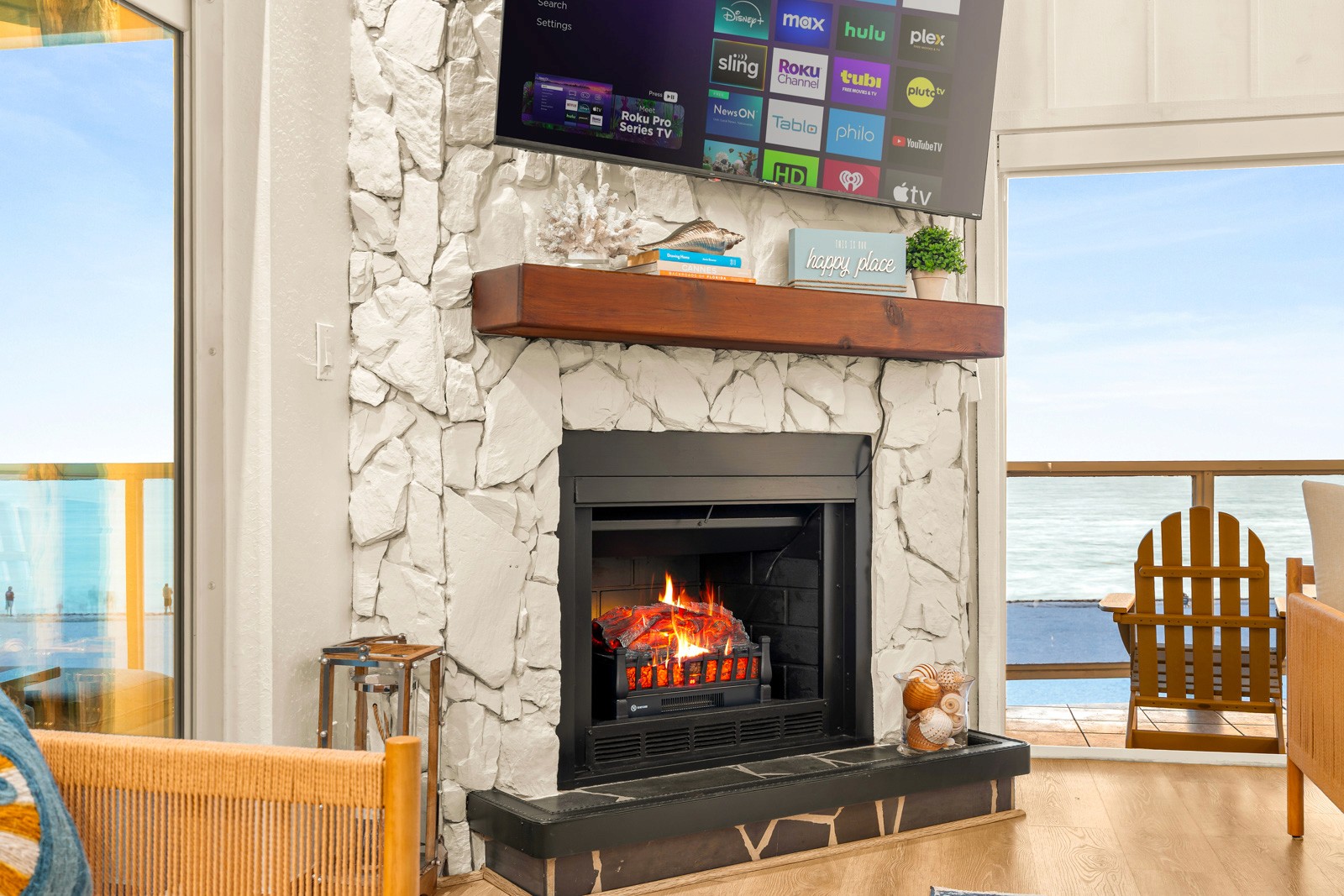 Beach house living area with white stone fireplace, wall-mounted TV and a balcony looking out to the Gulf, from a Gator Gaze Media shoot in Indian Shores