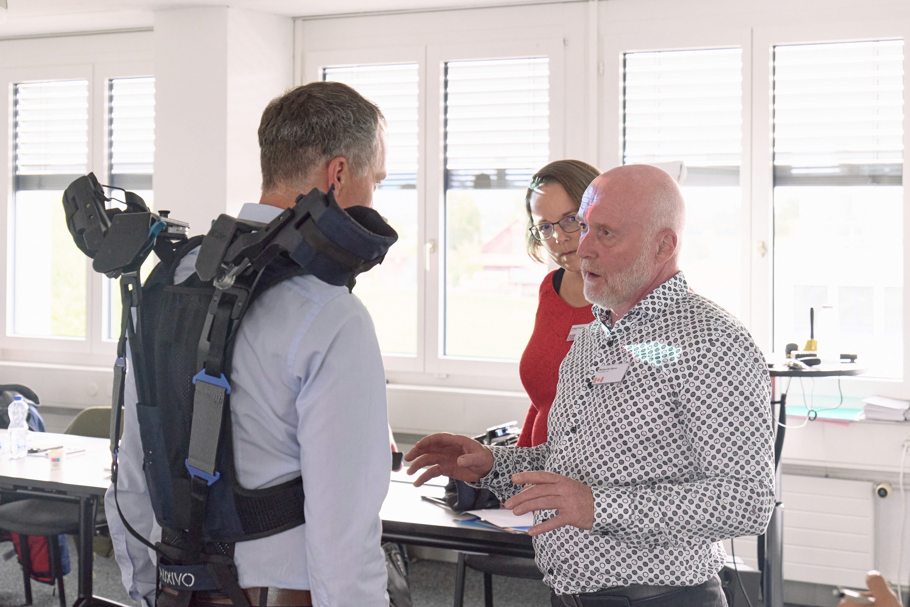 Démonstration d'un exosquelette industriel Auxivo lors d'un séminaire de formateurs, avec un spécialiste expliquant le dispositif à deux participants.