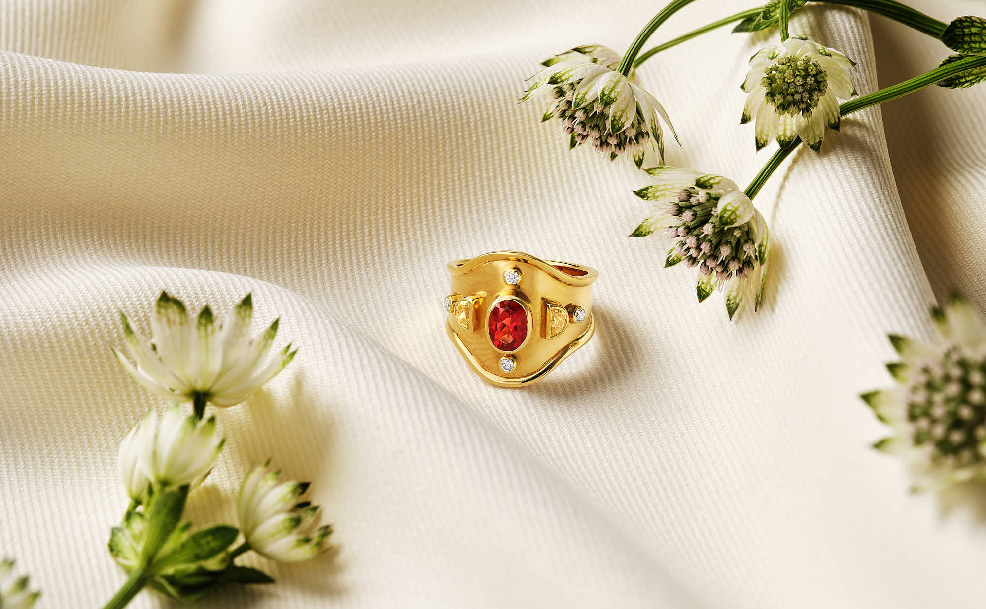 A close-up of a delicate arrangement featuring pink flowers, green leaves, and a small orange shell on a white fabric.