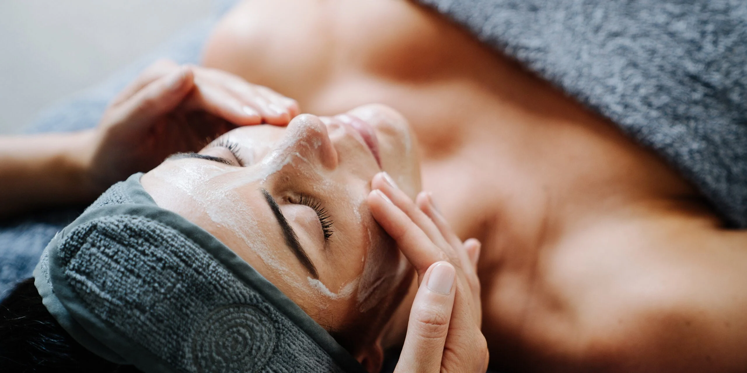 Woman with closed eyes receiving a facial treatment in a grey towel wrap, from the Endota Spa campaign