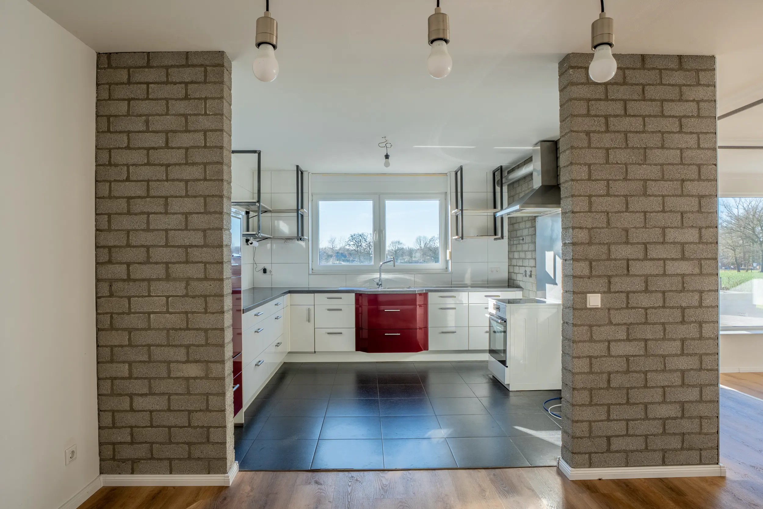 Offener Wohn- und Küchenbereich mit Klinker-Stützpfeilern, Eichenparkett und roten Farbakzenten im Einfamilienhaus Ochtrup