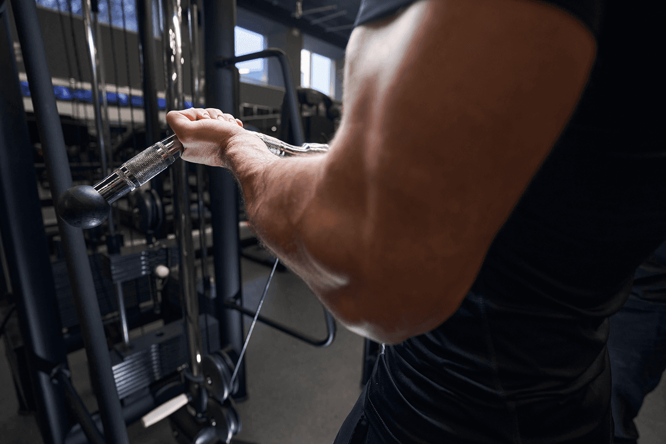 Close-up of a man performing a cable curl on a gym machine, focusing on his arm muscles.