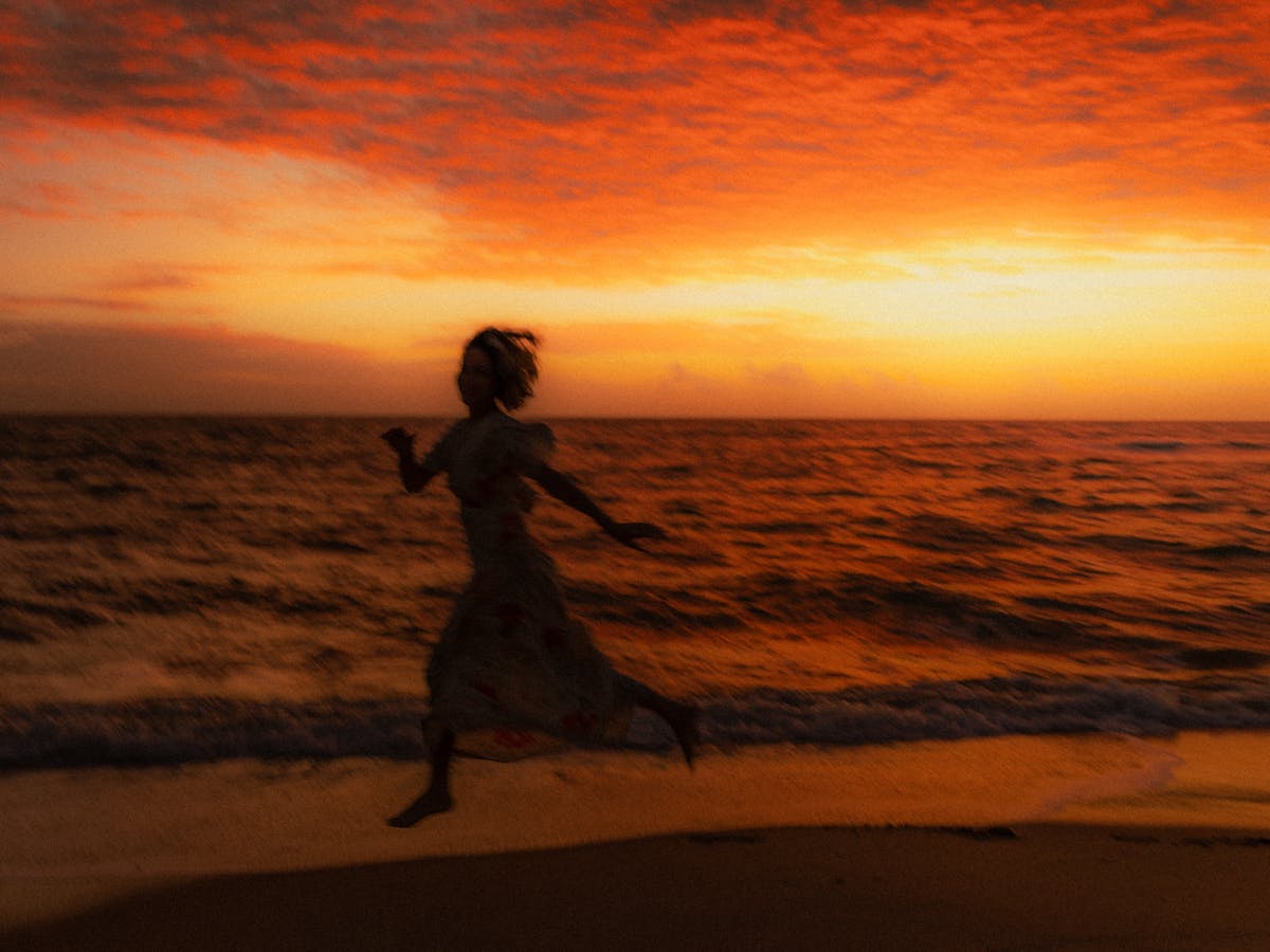 Woman silhouetted against a dramatic red sunset, running along the beach