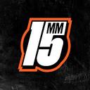 Young man with brown hair and blue eyes in an urban setting with graffiti background, wearing a dark jacket and chain necklace.