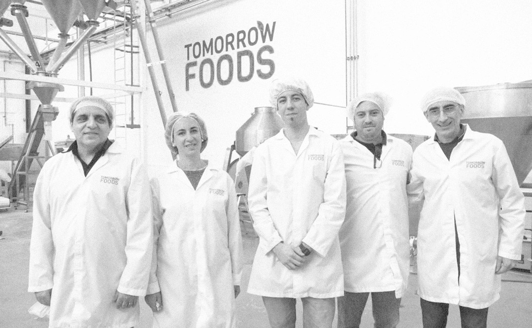Group in lab coats and hairnets inside a food production facility with industrial equipment.
