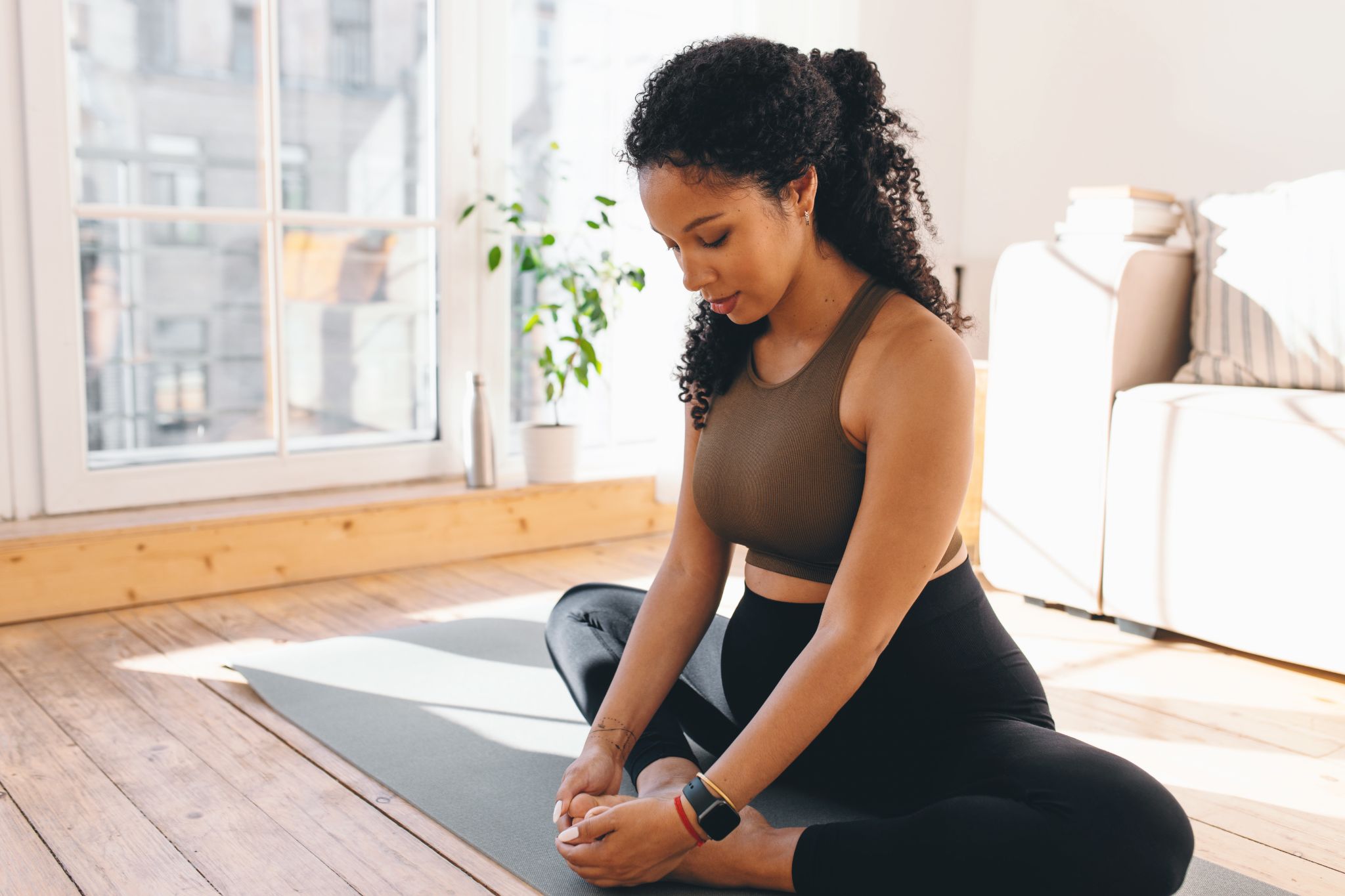 Pregnant woman practicing a seated bound angle yoga pose on a mat at home.