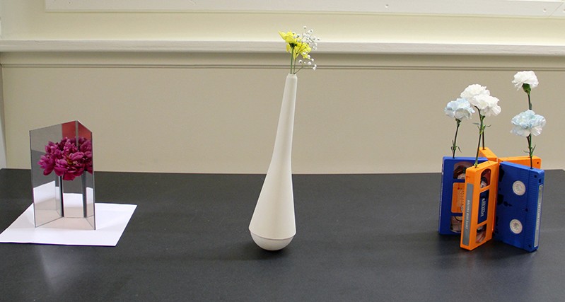 still nature on a table with flowers held in a tall vase, on videotapes, and glued on a reflective metal sheet