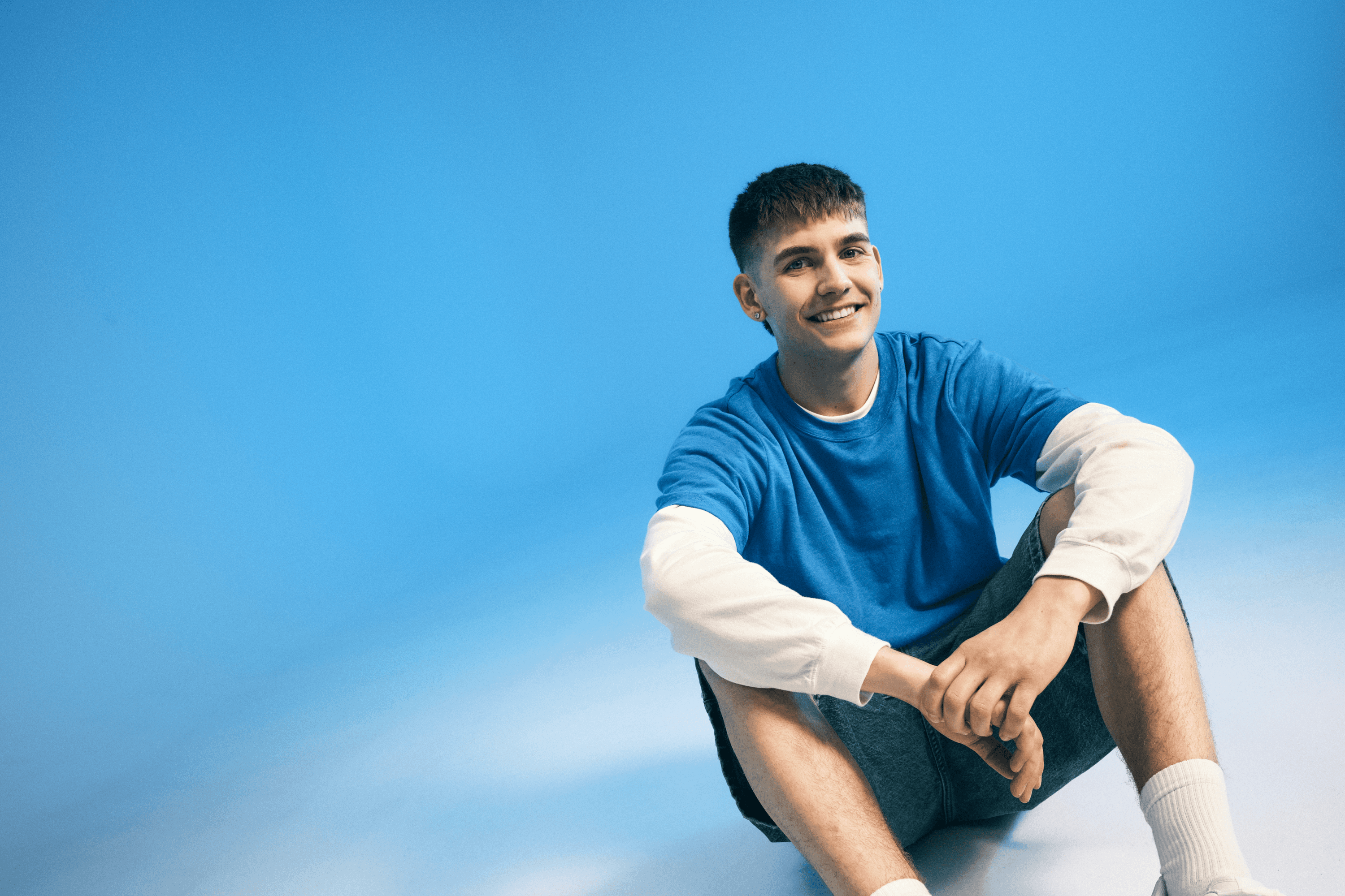 Model in a blue sweatshirt seated against a matching blue studio backdrop