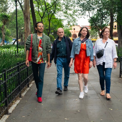 Grupo ng mga manlalakbay na naglalakad sa masiglang parke ng Coyoacan, niyayakap ang lokal na kultura.