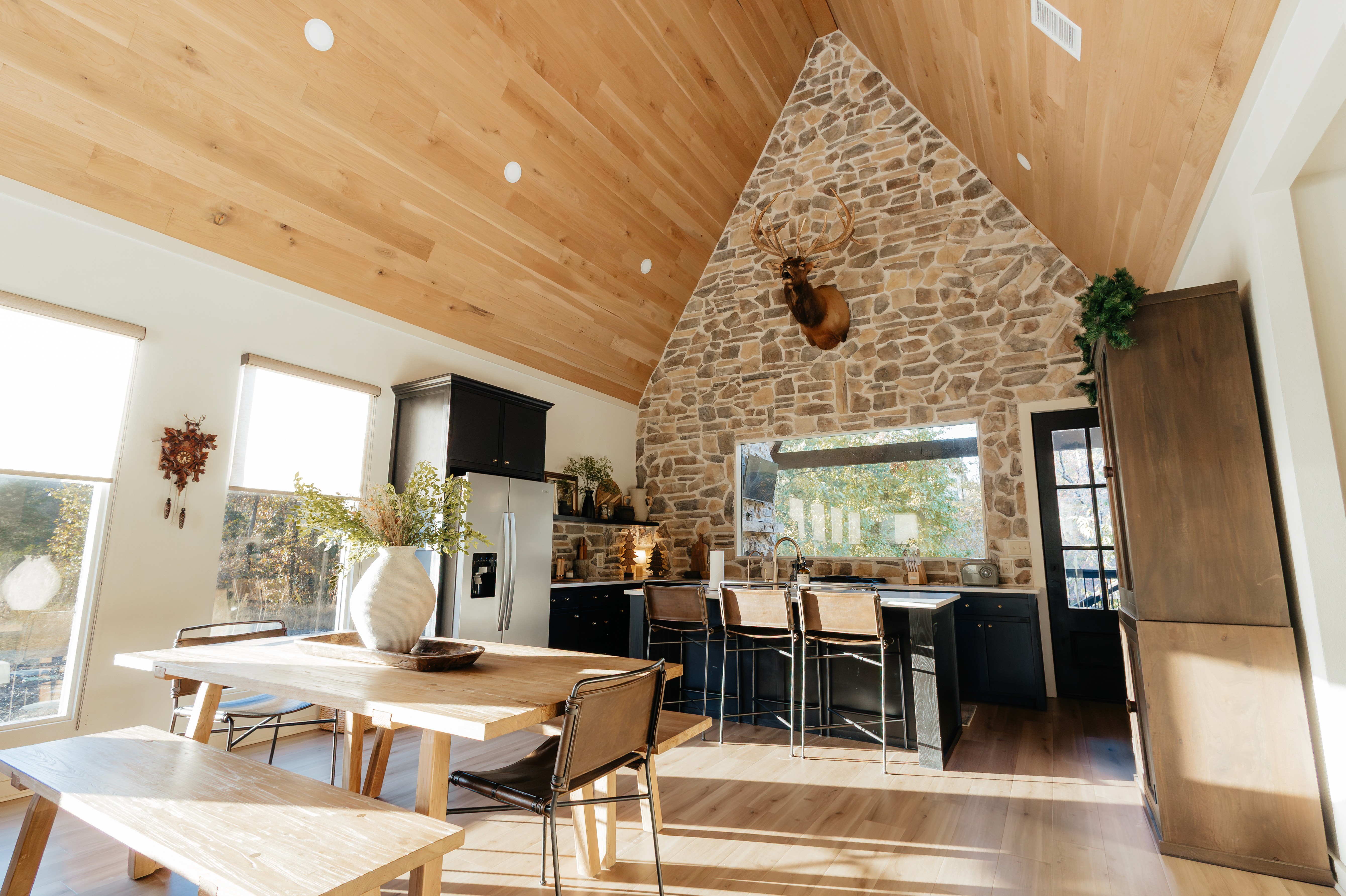 Wide shot of cozy modern cabin with light coming in from the side and cascading across the table with a elk taxedermy hung over the kitchen