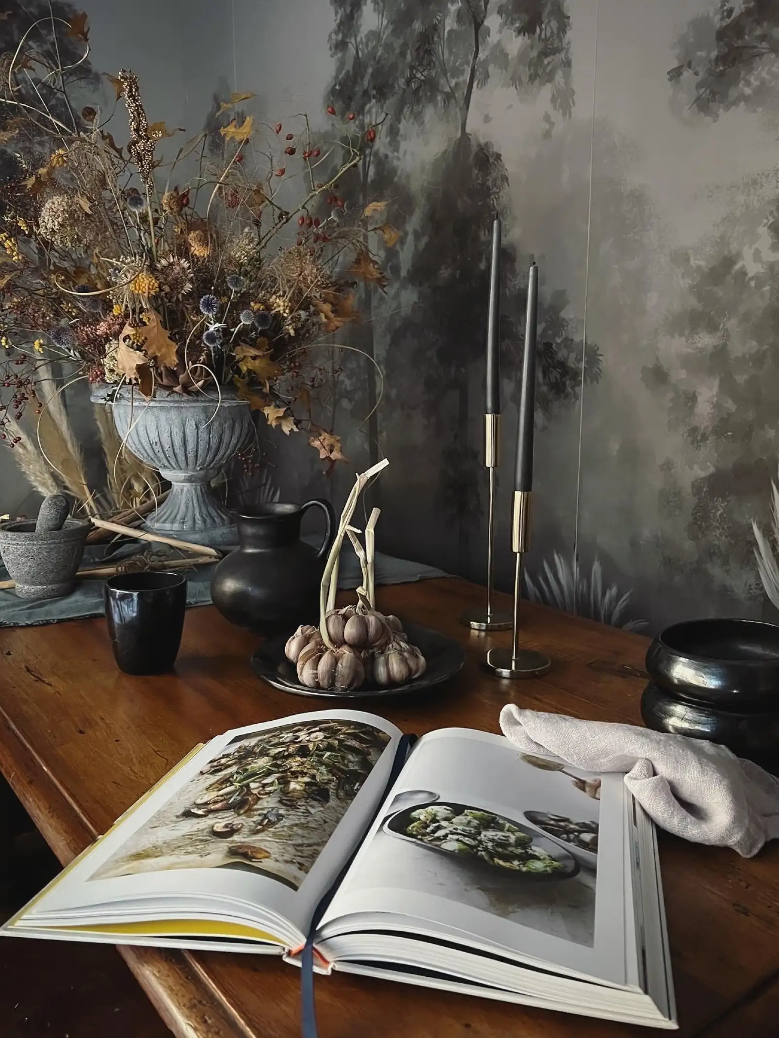 Fotografía de mesa rústica con flores secas, libro abierto y velas decorativas para inspiración en diseño interior natural.