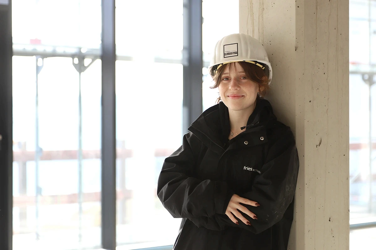 Fries Architekten – Bauzeichnerin mit Helm steht auf Baustelle.
