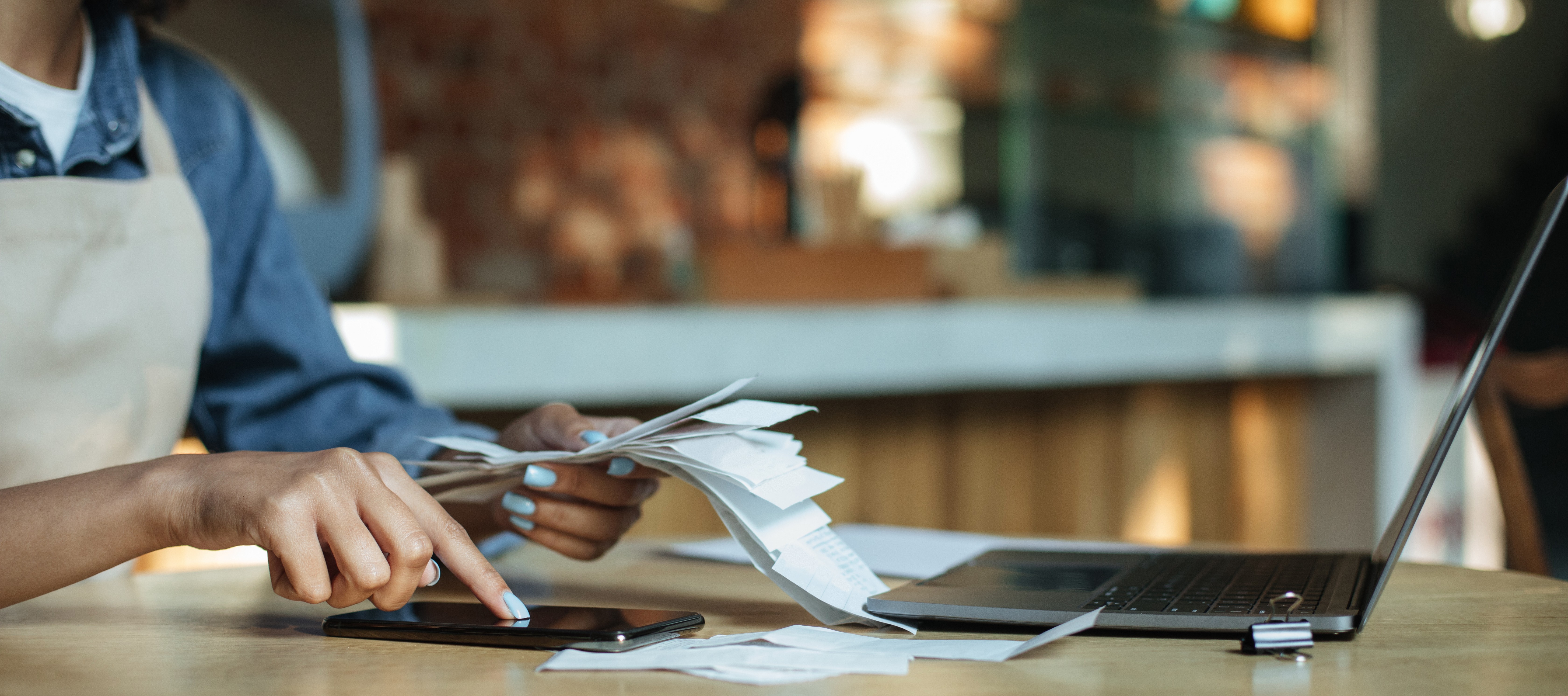 a person organizing receipts with phone and laptop