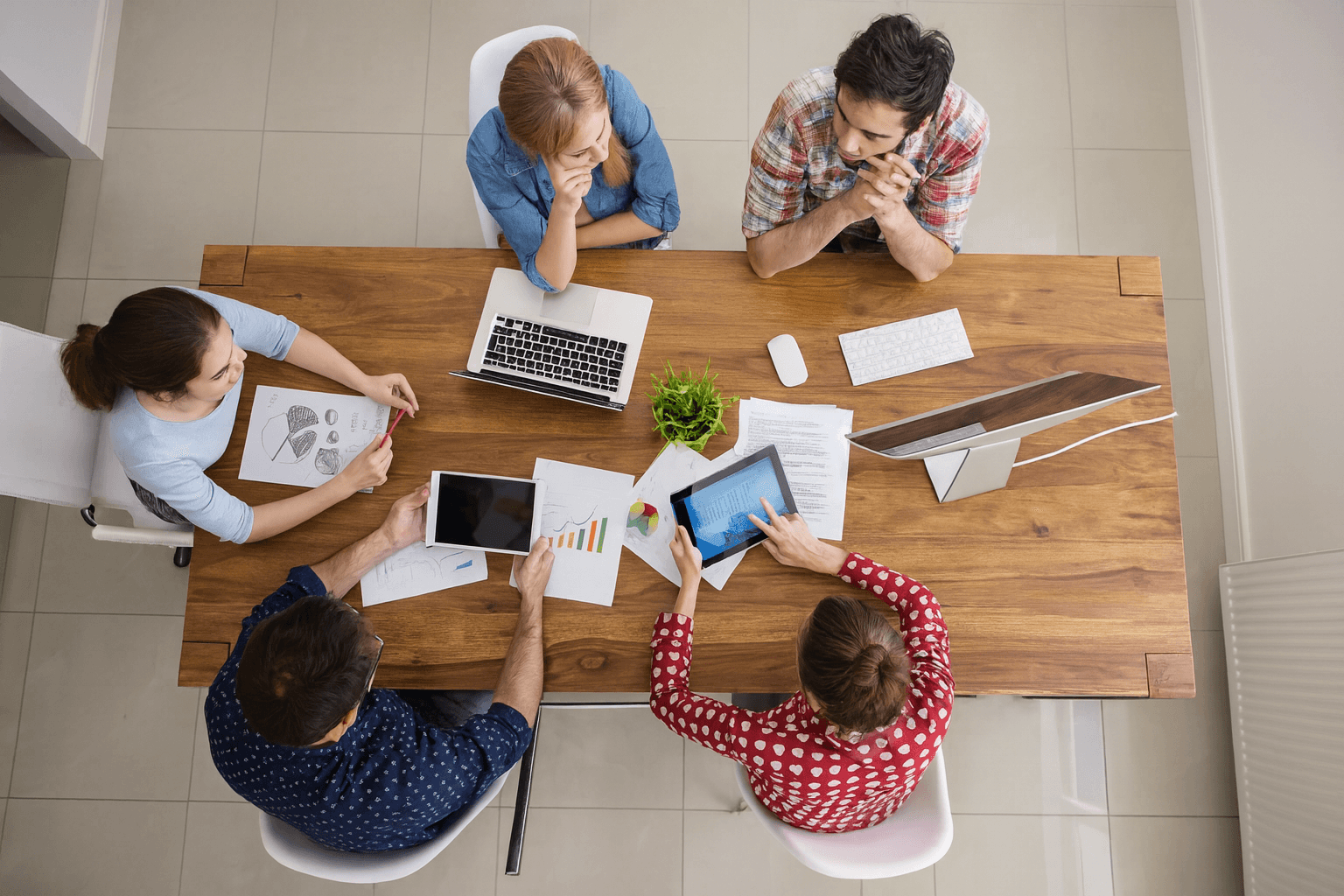 Un groupe de personnes travaillant ensemble autour d’une table avec des ordinateurs, tablettes et documents, symbolisant la planification et la gestion des campagnes publicitaires pour les Sponsored Products sur Amazon.
