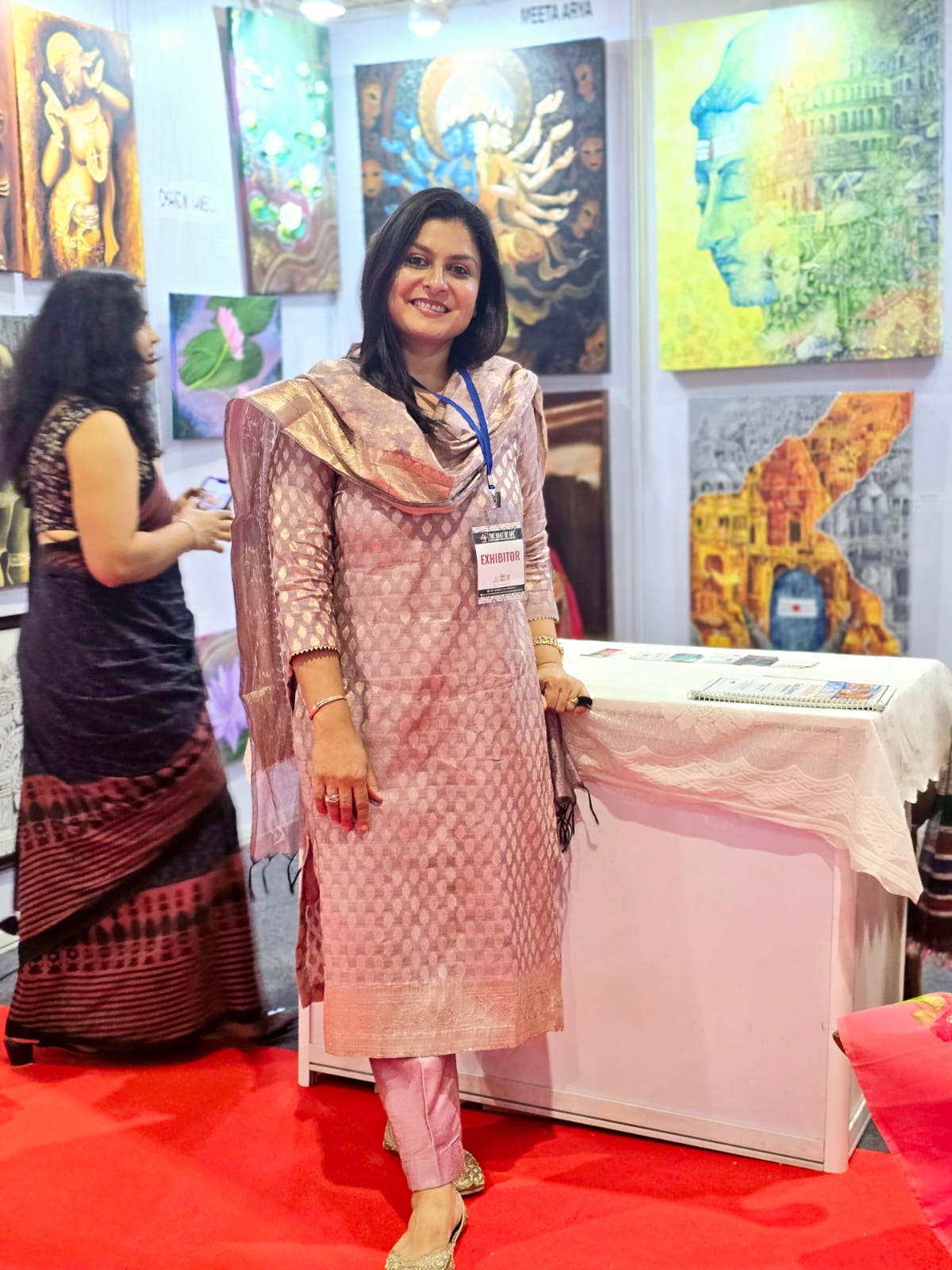 Mrs. Chandni Kamboj, founder of The Creative Pod, standing beside artworks at an art exhibition
