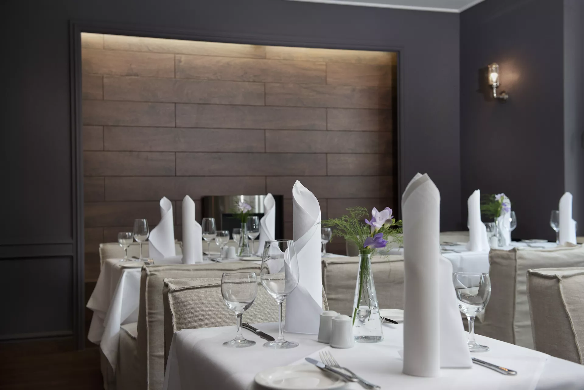 Ein eingedeckter Tisch im Restaurant mit Tischdecke, aufgestellten Servietten und einer kleinen Blume auf dem Tisch