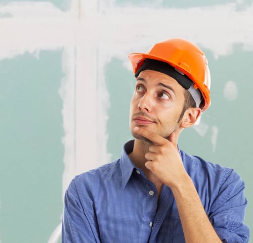 Persona con aria dubbiosa davanti parete di cartongesso quasi finita in appartamento