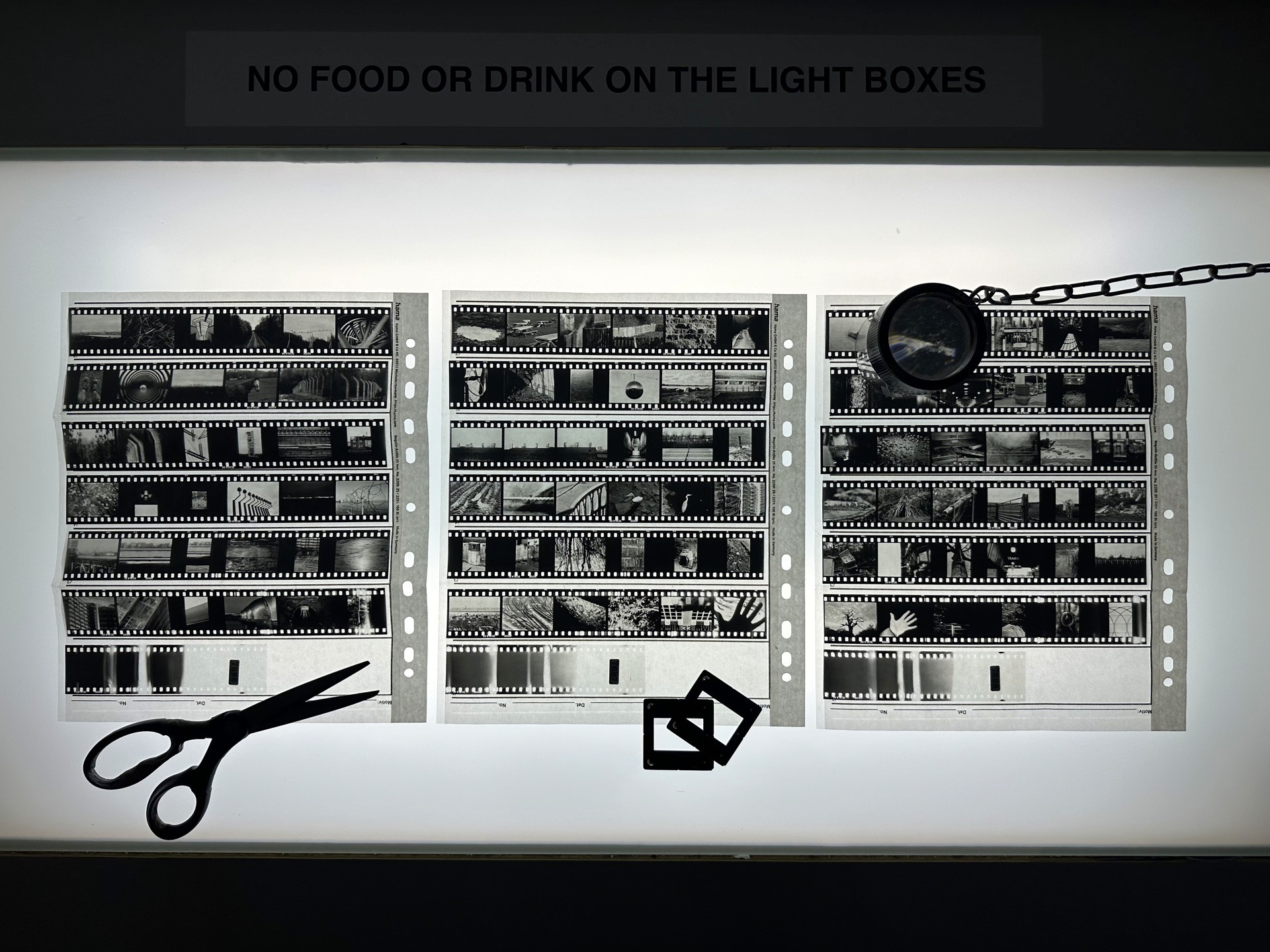 Strips of black and white slide film laid out on a light box, with scissors, slide mounts and a loupe on a chain.
