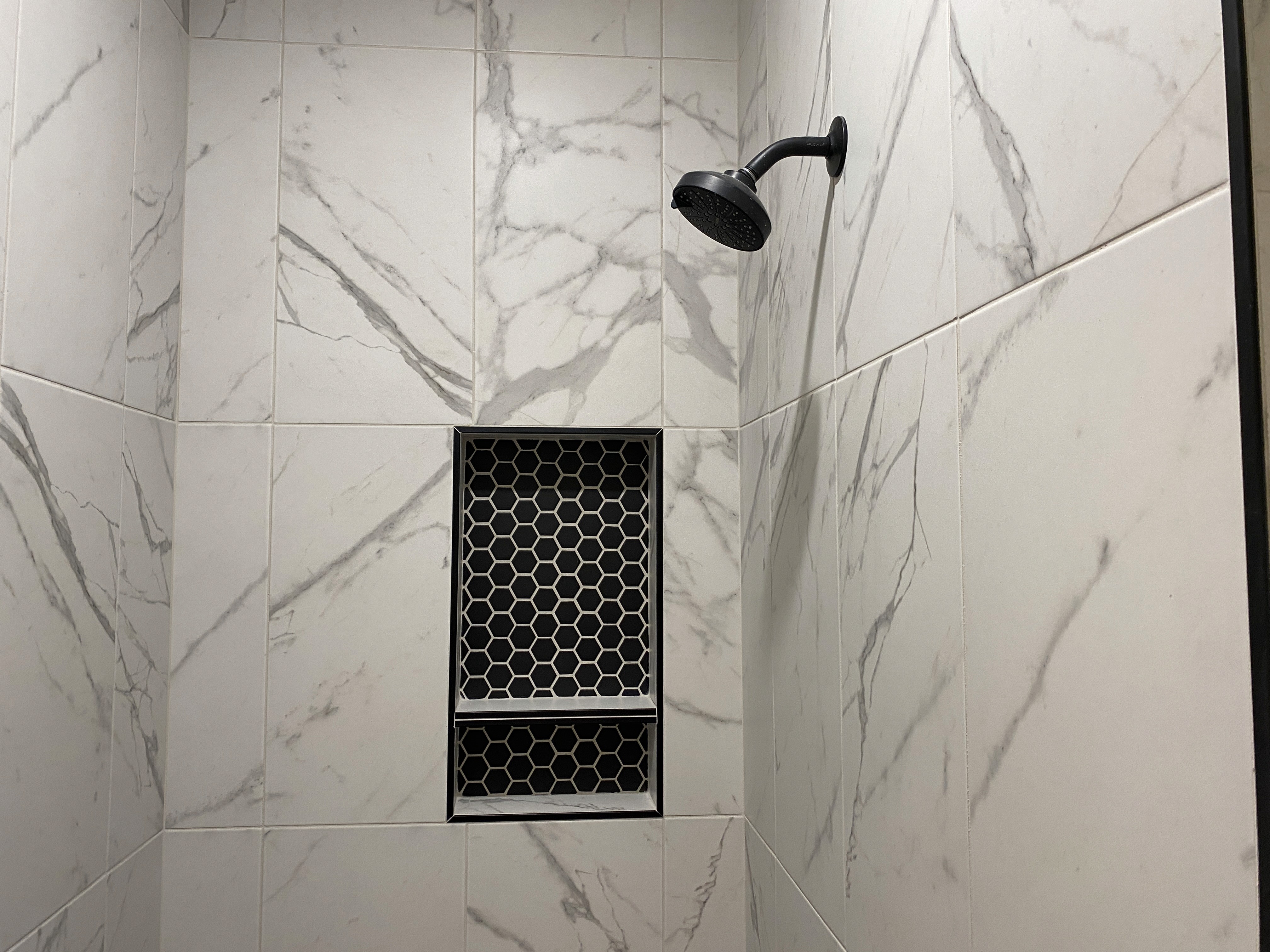 Primary bathroom shower in a duplex home with clean tile work and an accent niche.
