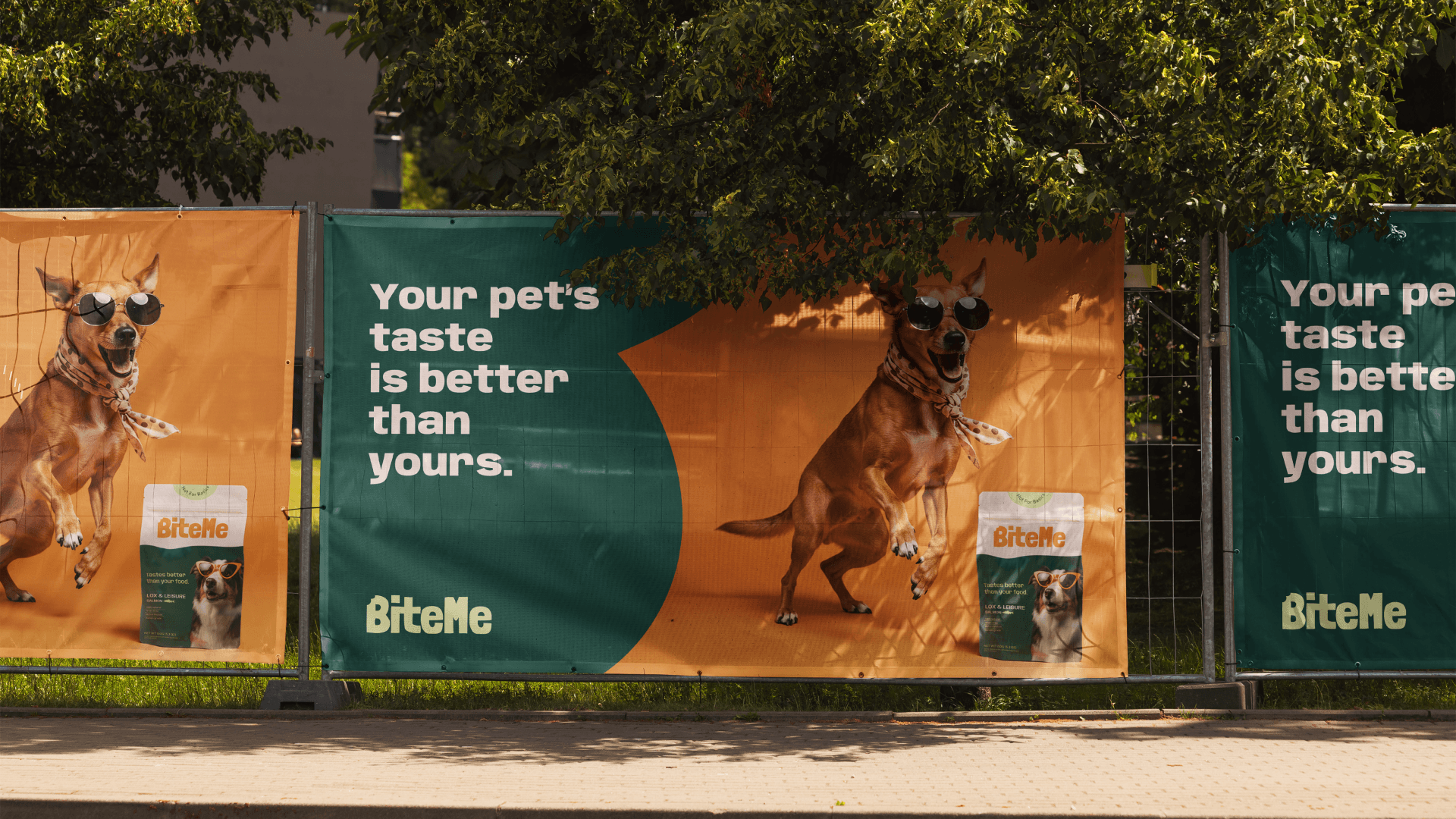 A series of outdoor banners display a playful dog wearing sunglasses, promoting "BiteMe" pet food with the slogan "Your pet's taste is better than yours" against a bright green and orange background.