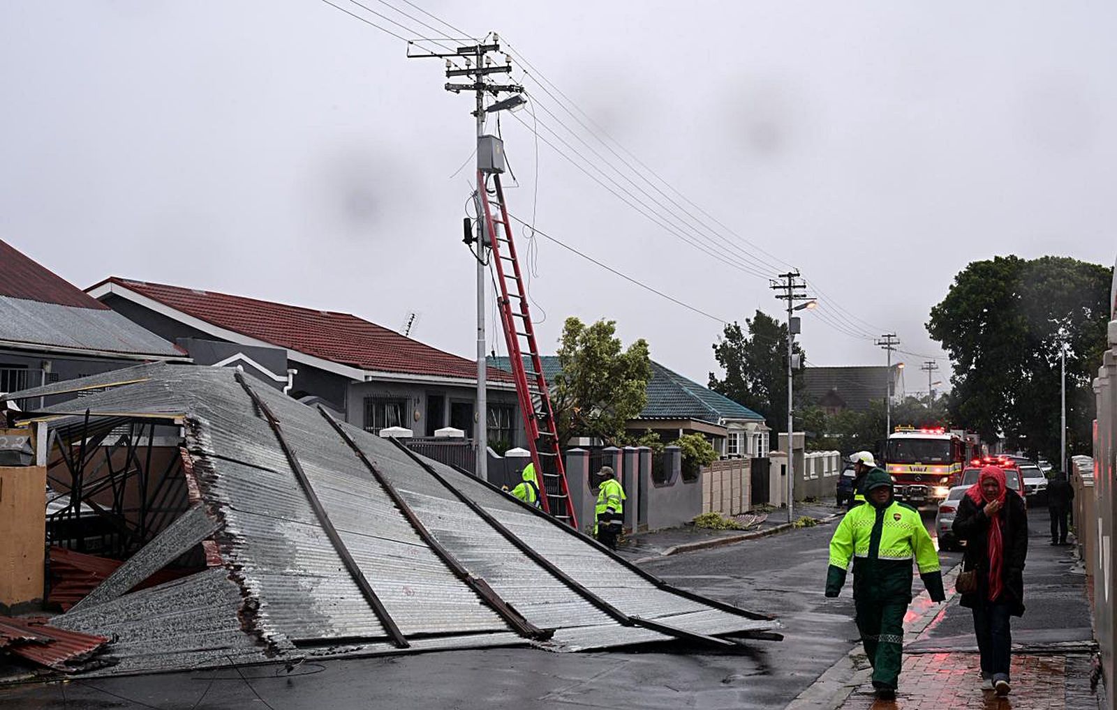 Roof laying in the road in a town with gloomy skies and emergency workers and equipment on the scene