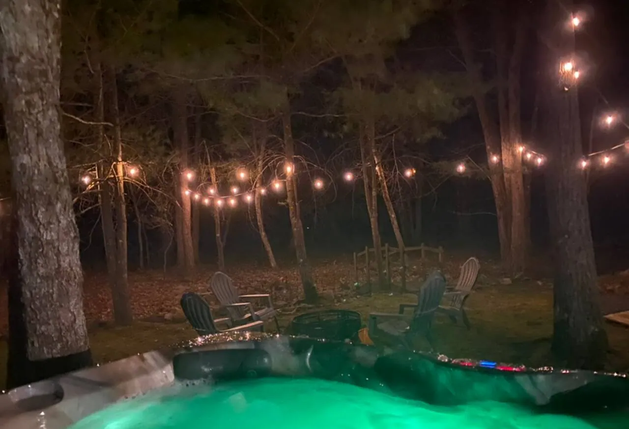Hot tub lit green at night under string lights over the backyard at Relax in Style, Lake Harmony
