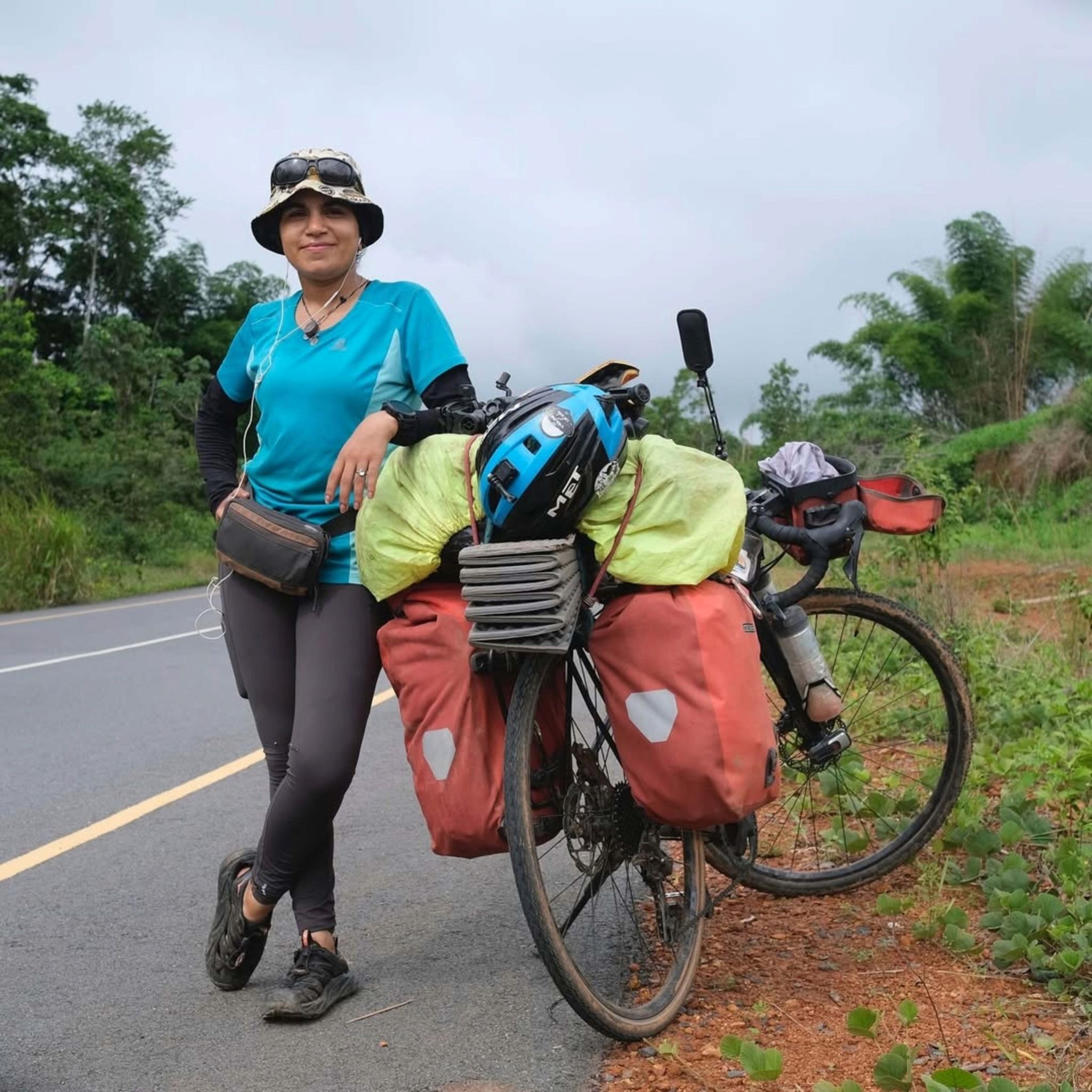 A woman standing at the side of the road leaning on her heavily loaded bicycle. She is bikepacking through Africa alone.
