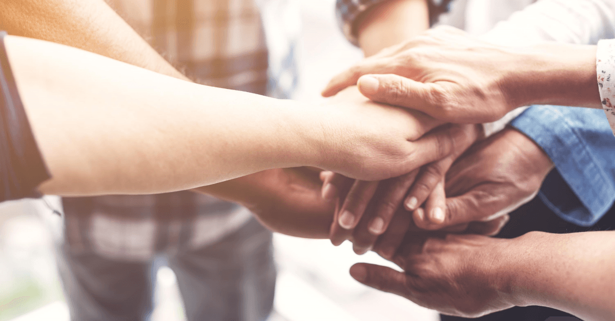 Several people put their hands together in a team building exercise to cheer each other on and inspire hope.