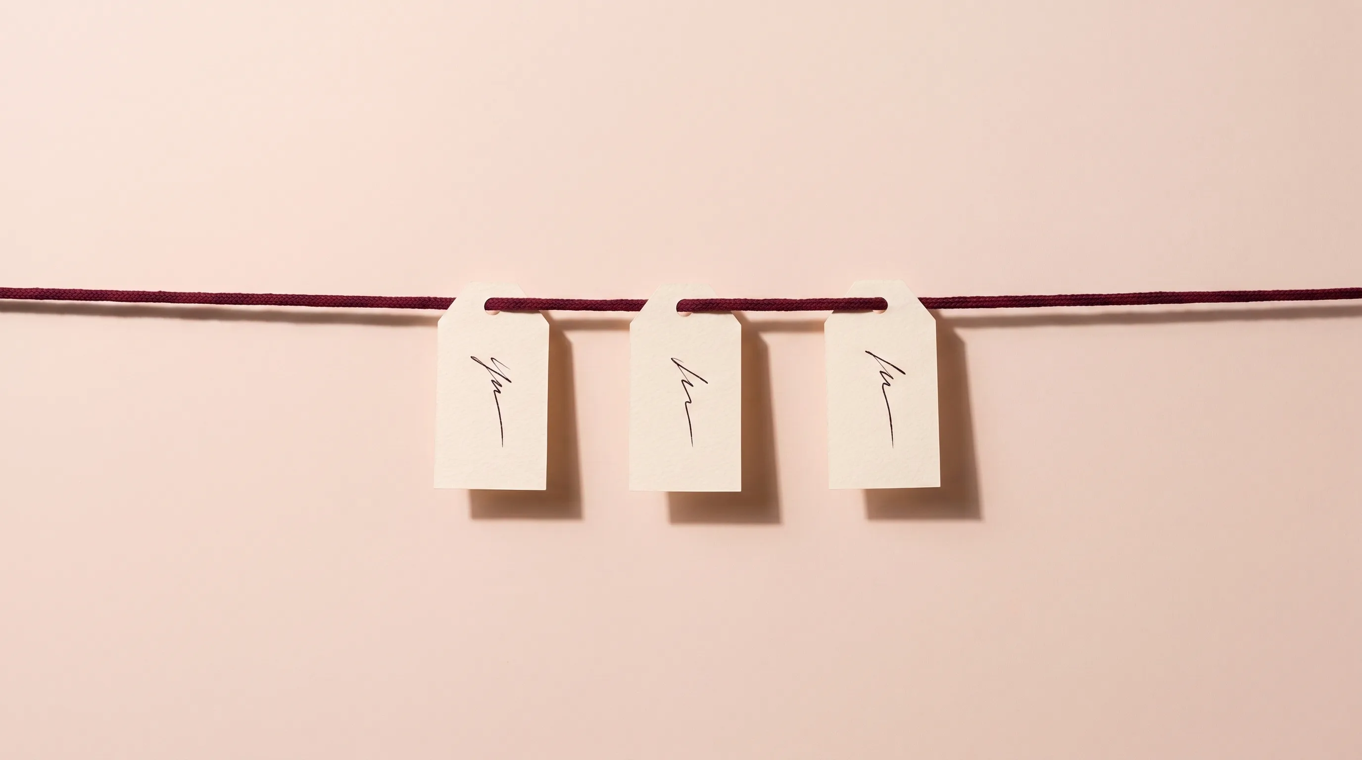 Three paper tags hanging from a taut cord, evenly spaced, each carrying a single ink mark