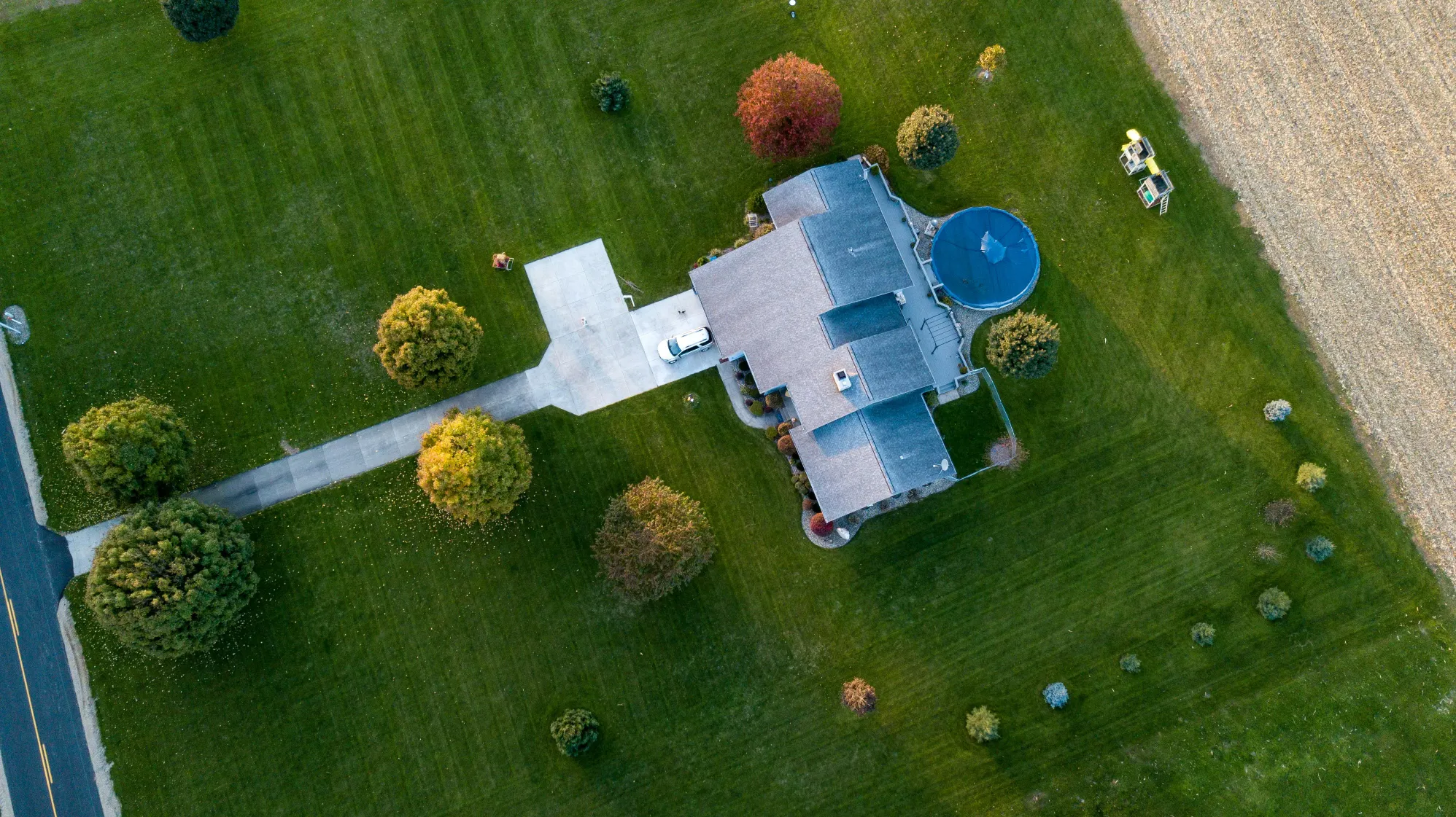 Top down aerial view of a large residential property with a long driveway, expansive lawn, and a round above ground pool in the backyard. This real estate drone photography clearly shows the full property layout and outdoor features, giving a drone photographer strong visual context for marketing spacious homes.