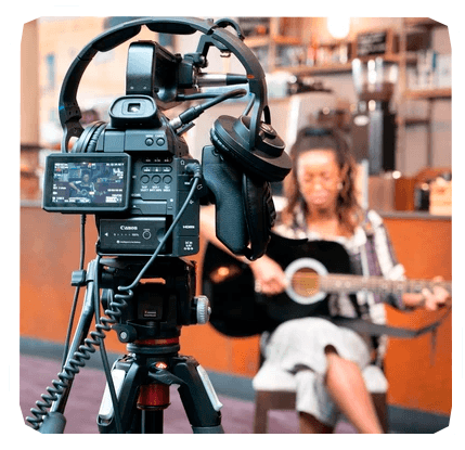 Photograph of a professional camera recording a female musician in the background