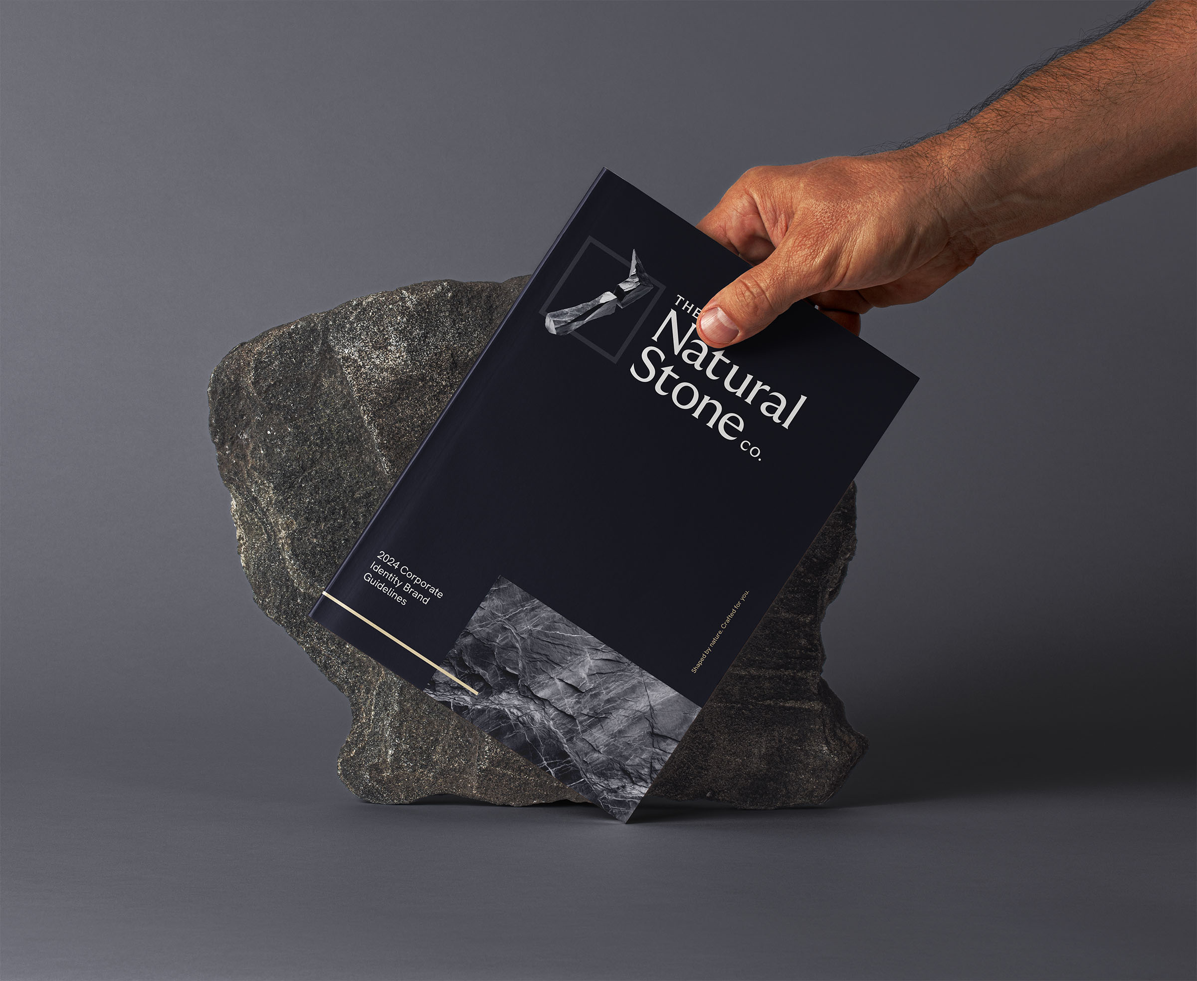 Natural Stone Company brand guidelines booklet being held by a male hand