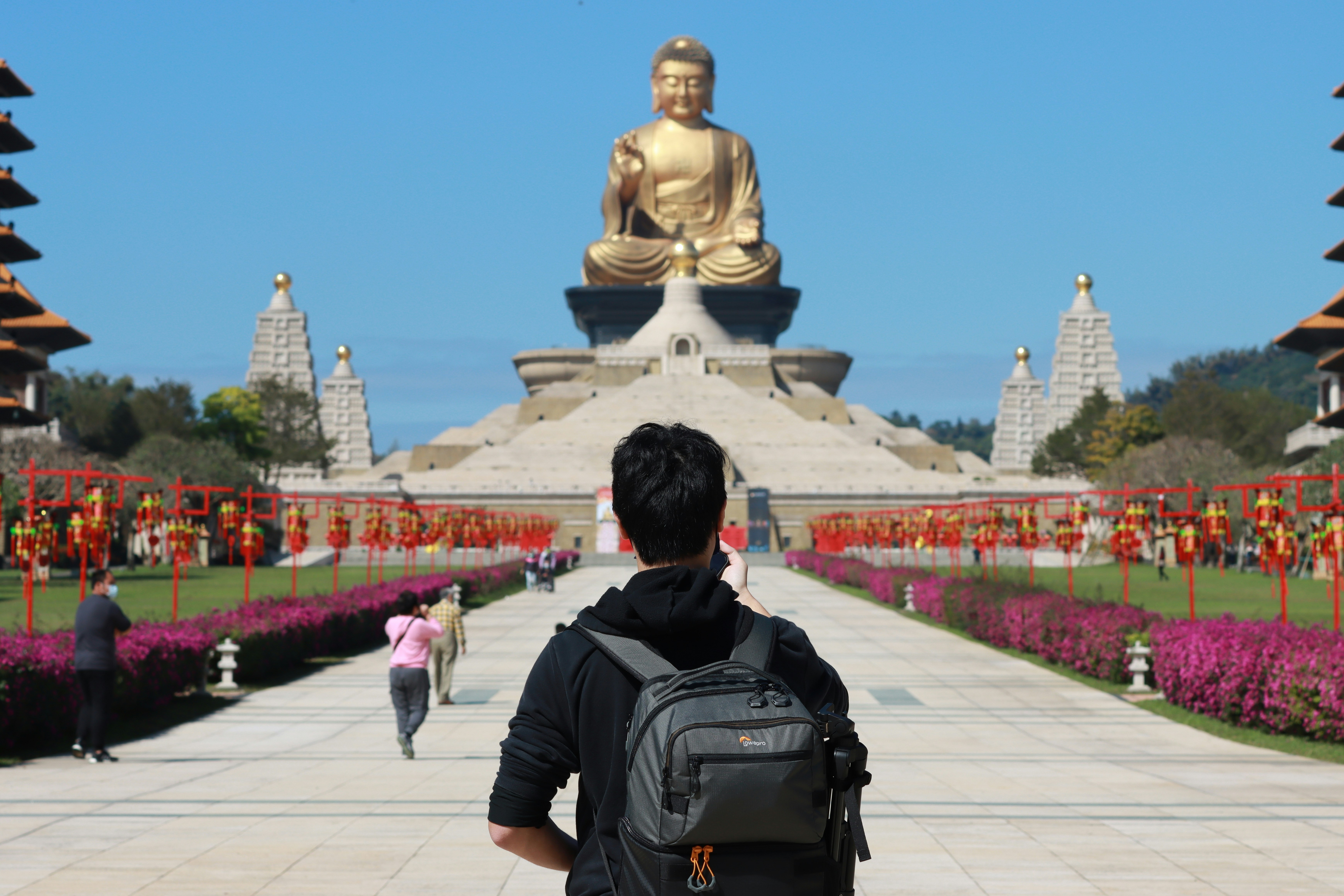 a man with a backpack looking at a large buddha statue