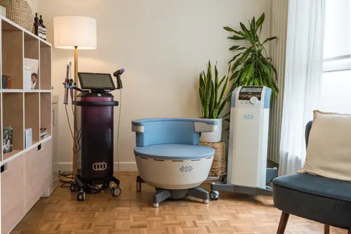 Modern wellness clinic room featuring an Emsella chair, BTL medical devices, and relaxing interior décor with plants and natural light.