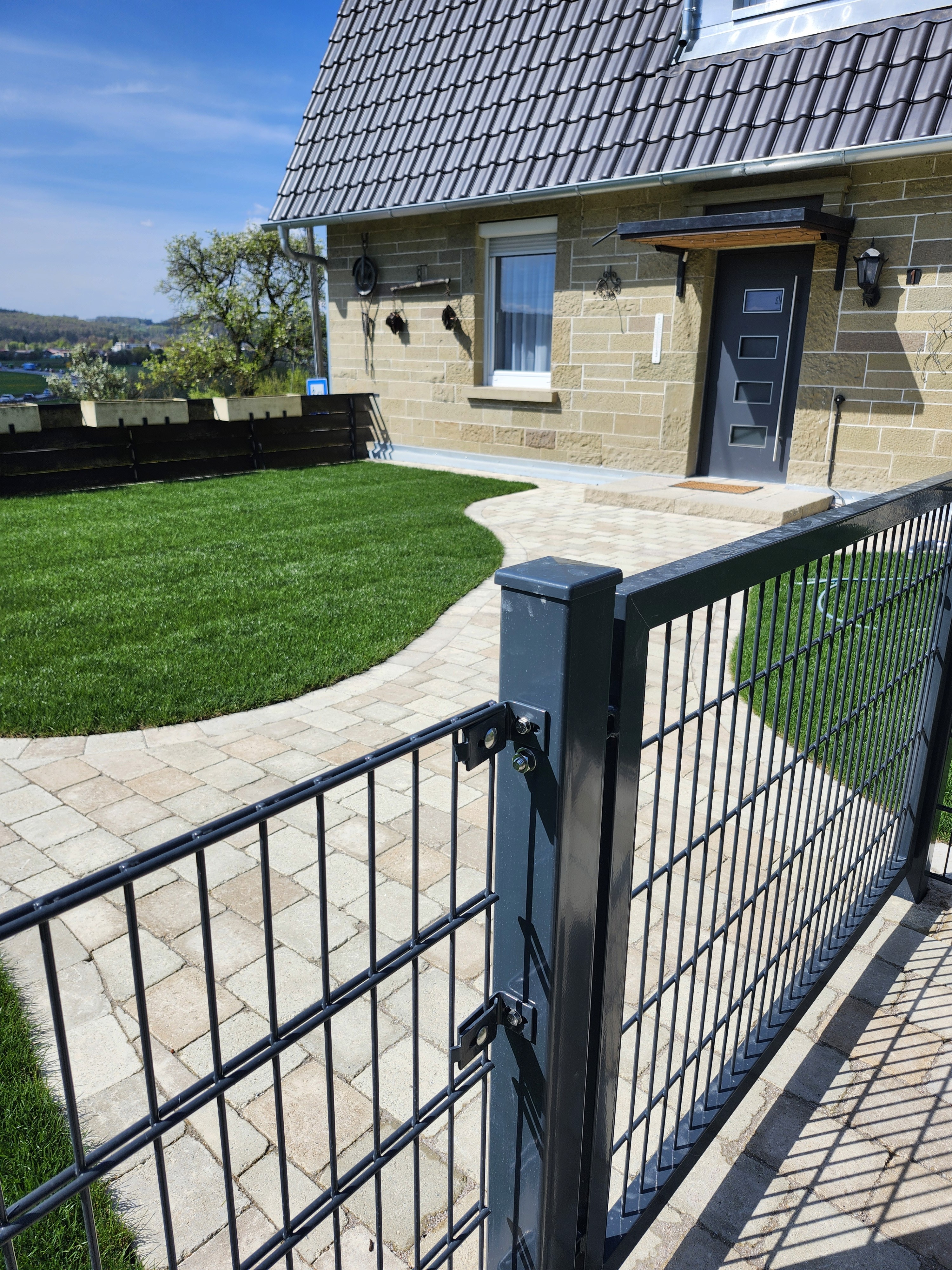 Gartenweg mit Metallzaun, gepflasterter Eingang und Haus aus Sandstein von Marohn & Binder im Gartenbau. , Marohn & Binder Gartenbau